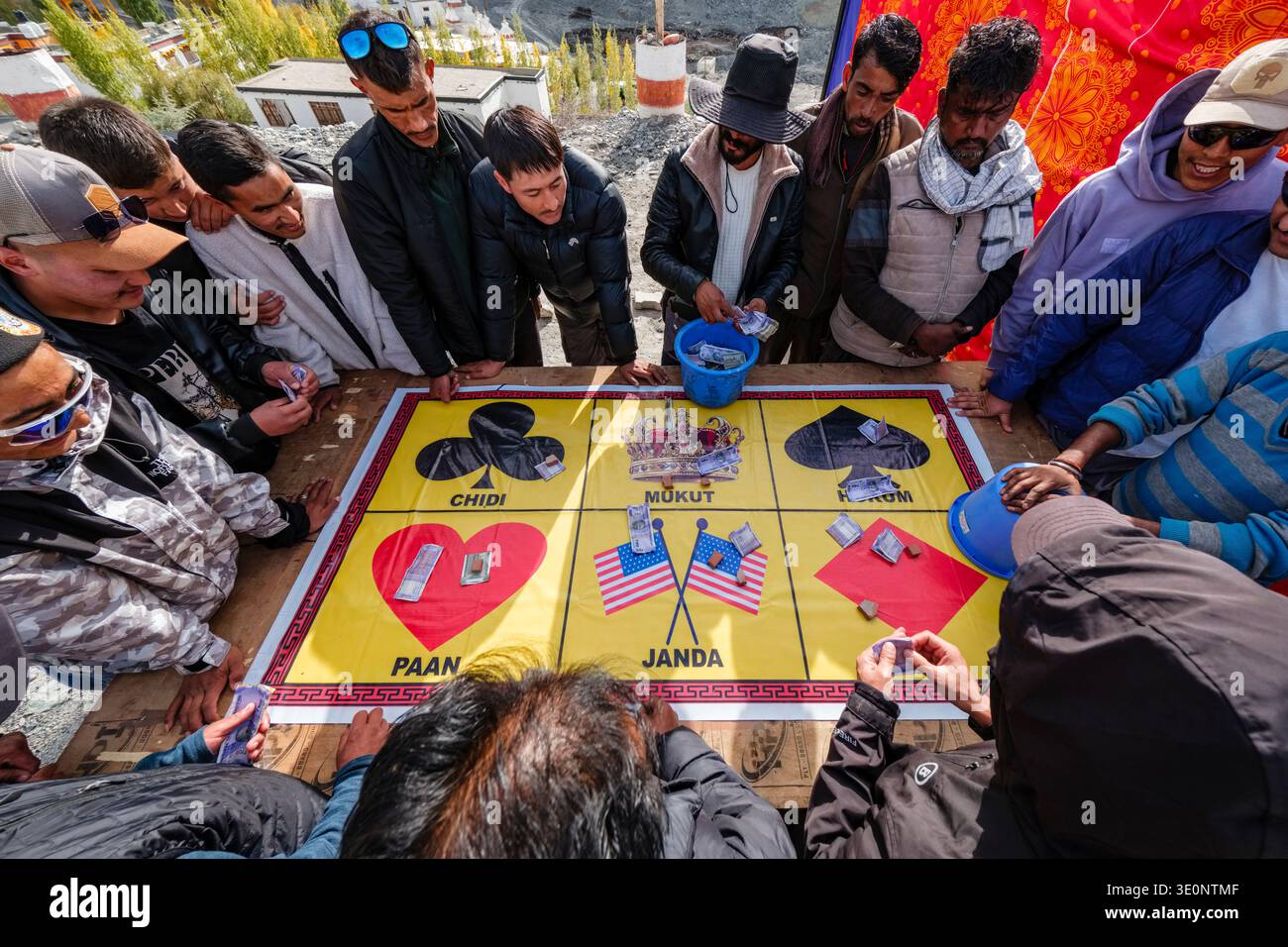 Men gather around a vibrant Jhandi Munda gambling mat to place bets during the public festivities of Diskit Gustor. Stock Photo