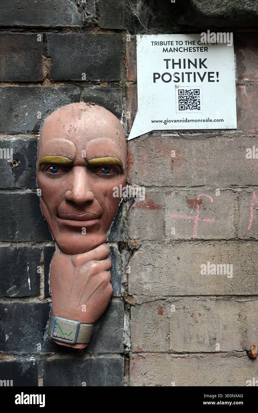 Wall-mounted sculpted head and ‘Think Positive’ QR code sign beneath Manchester Oxford Road railway station, Manchester, England, UK. Stock Photo