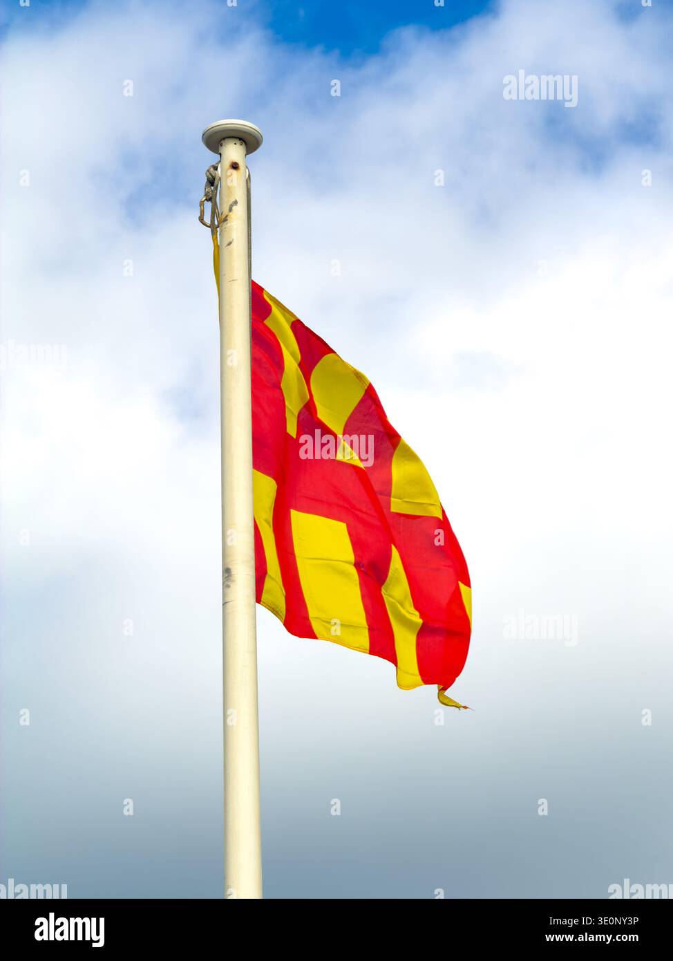 northumberland flag featuring thick vertical red and yellow stripes waves from a light-colored flagpole against a bright, cloudy expanse - Smartphone Captured Stock Image