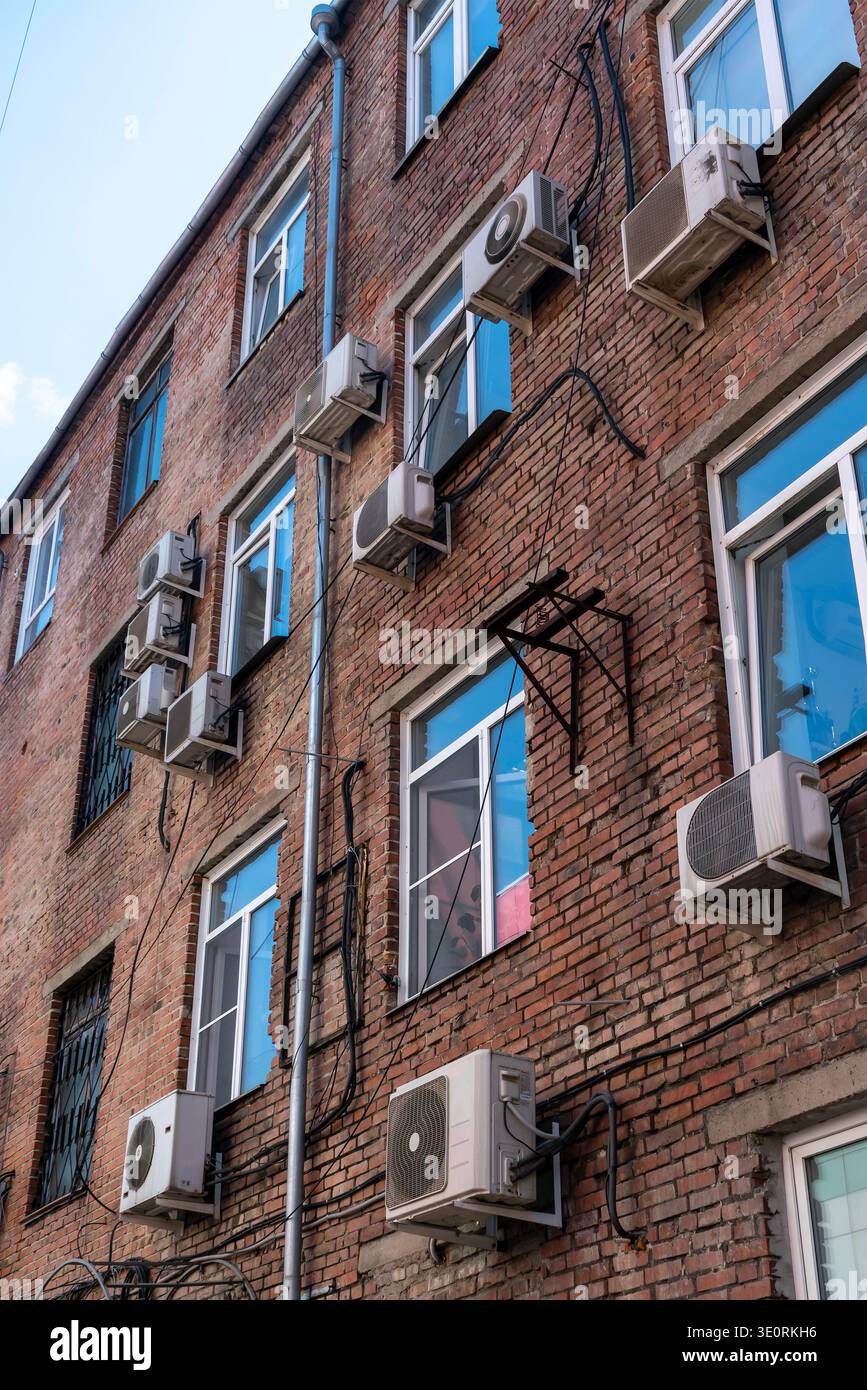 Rows of wall-mounted air conditioner units cover a red brick apartment ...