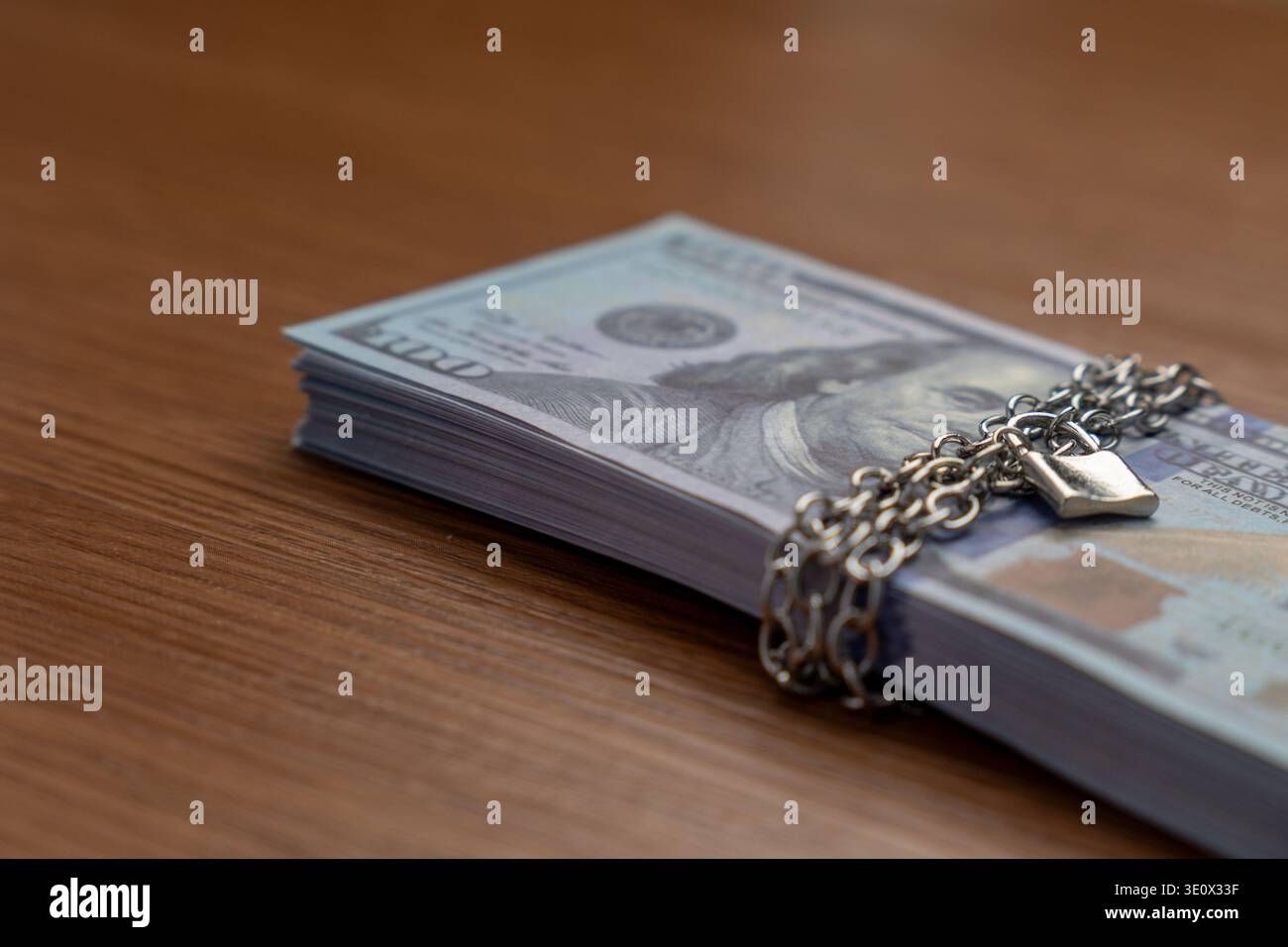 A bundle of one hundred US dollar bills bound with a metal chain and secured with a padlock. Financial security, asset protection, frozen accounts Stock Photo