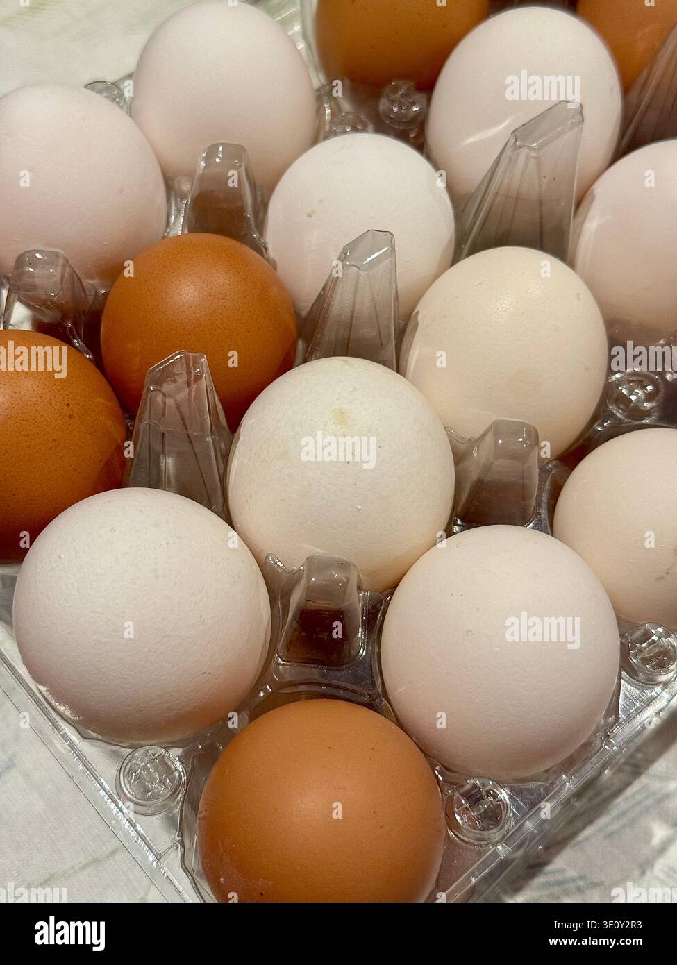 High angle close-up of mixed brown and white organic chicken eggs in a transparent plastic carton. - Smartphone Captured Stock Image