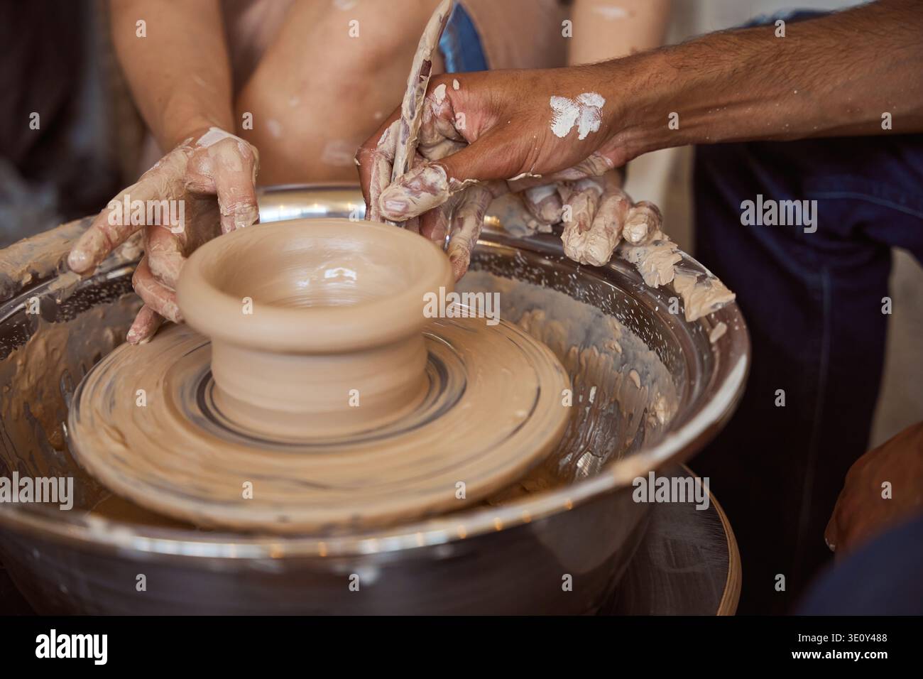 Two adults creating pottery on spinning wheel in workshop Stock Photo