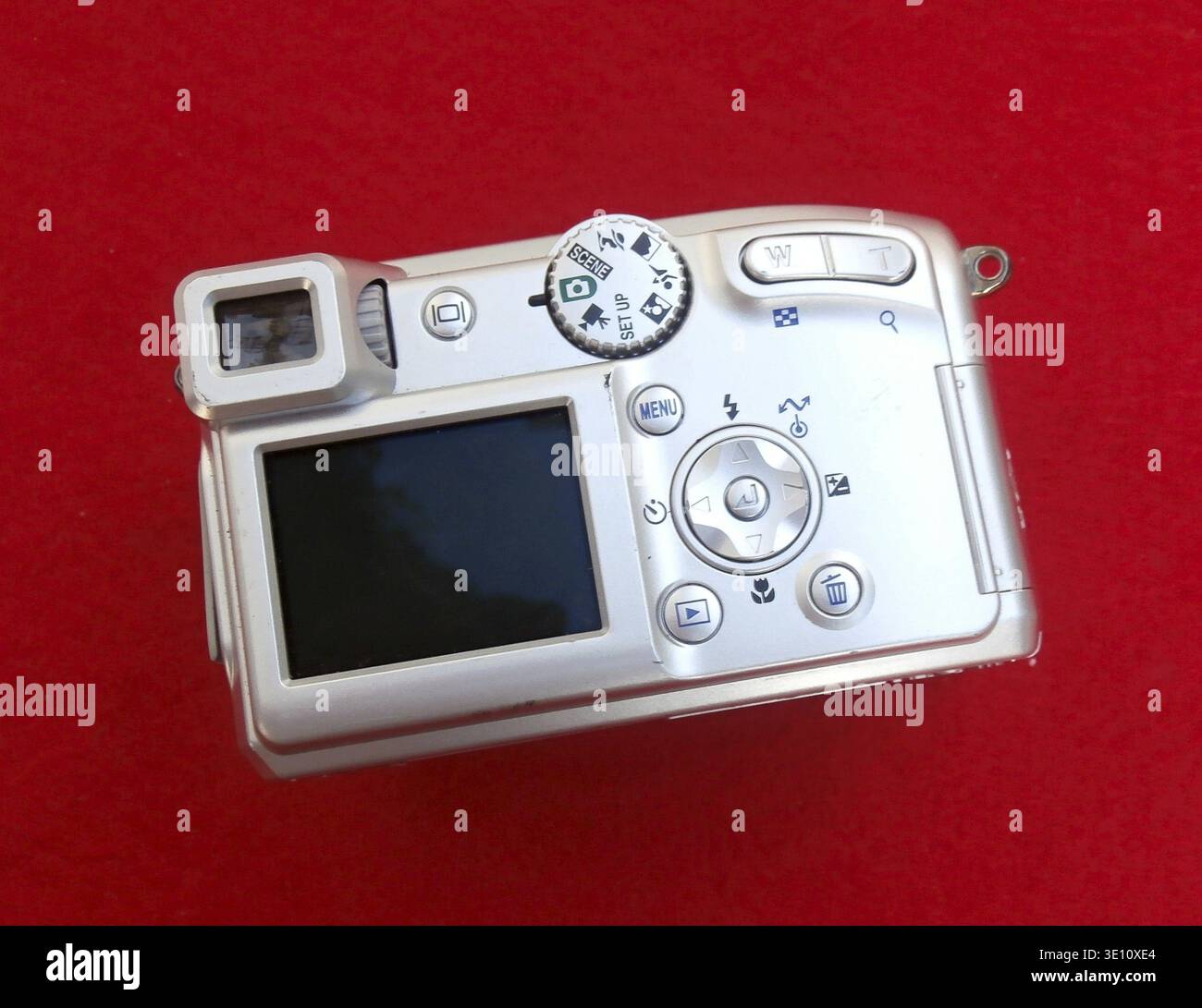 Silver digital compact camera placed on a red background, showcasing its design and features Stock Photo