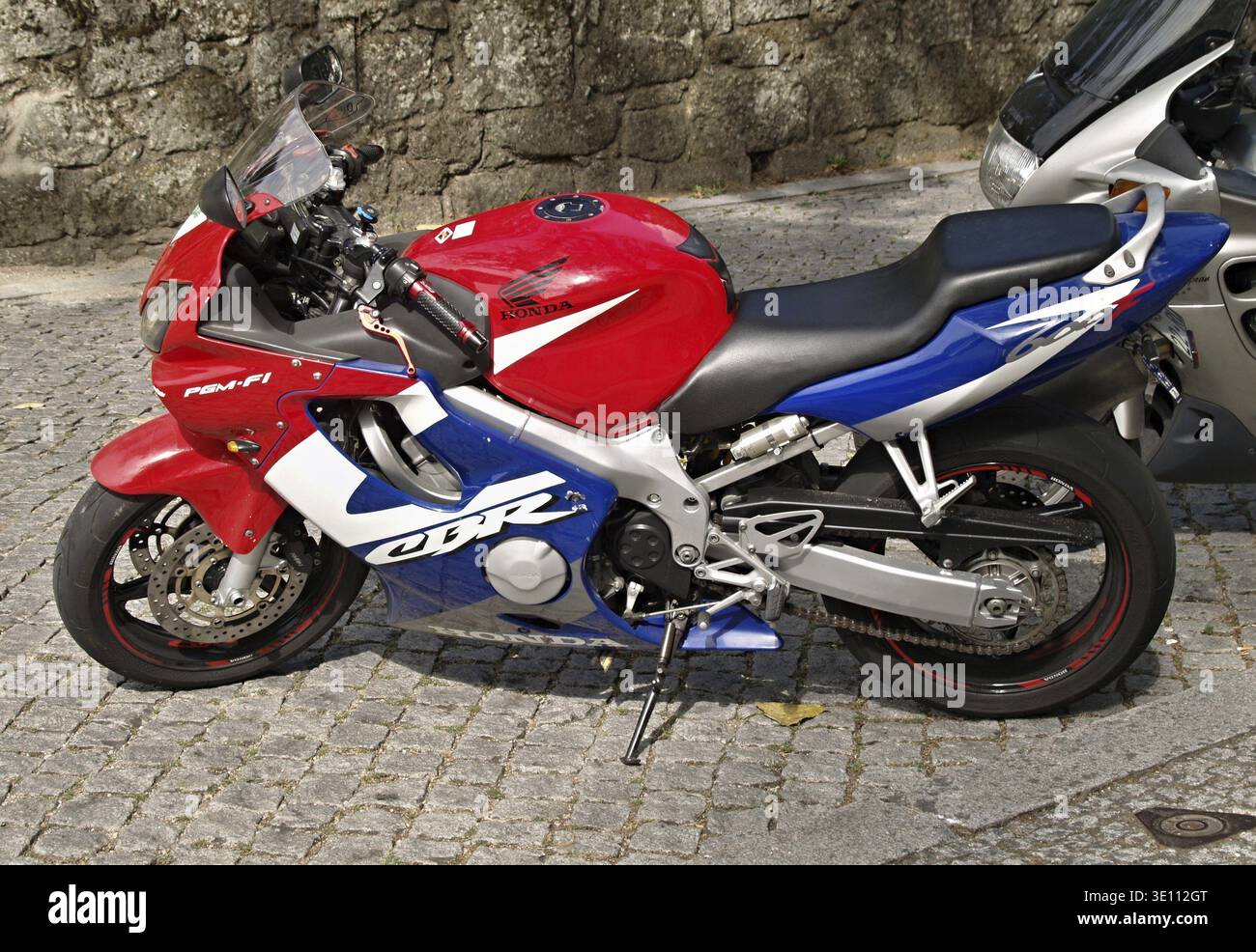 Red, white, and blue Honda CBR sport bike parked on a stone paved 