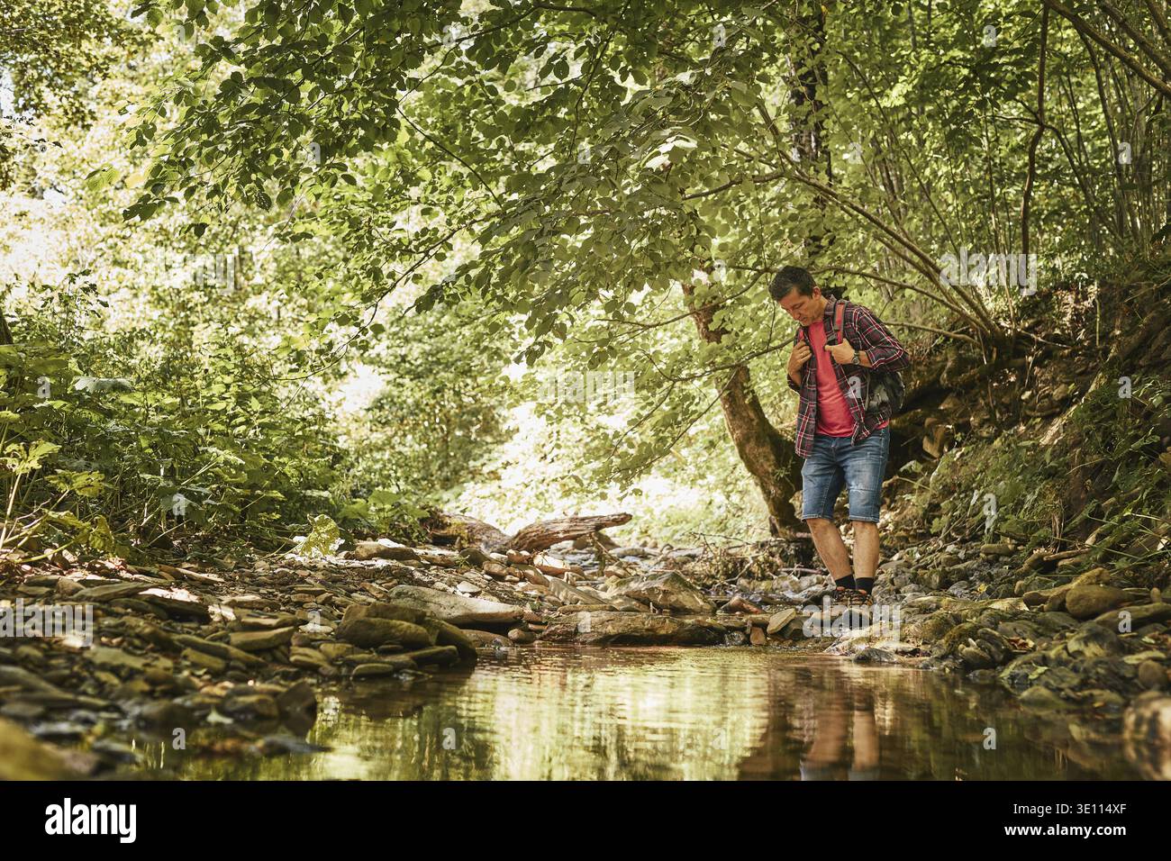 Trekking with backpack concept image. Backpacker in trekking boots crossing mountain river. Man hiking in mountains during summer trip. Vacation trip Stock Photo