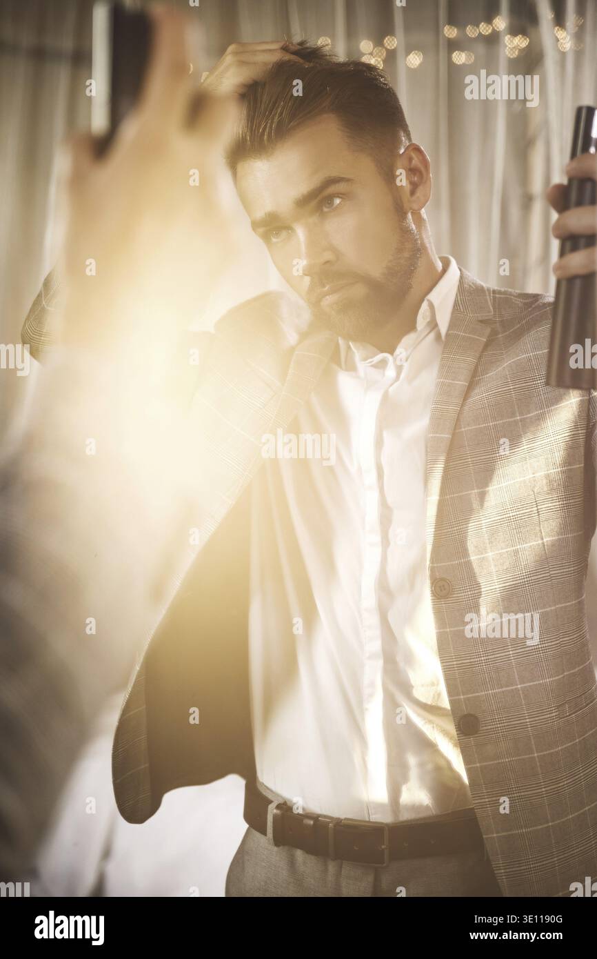 Young and handsome bearded man is using hairspray Stock Photo