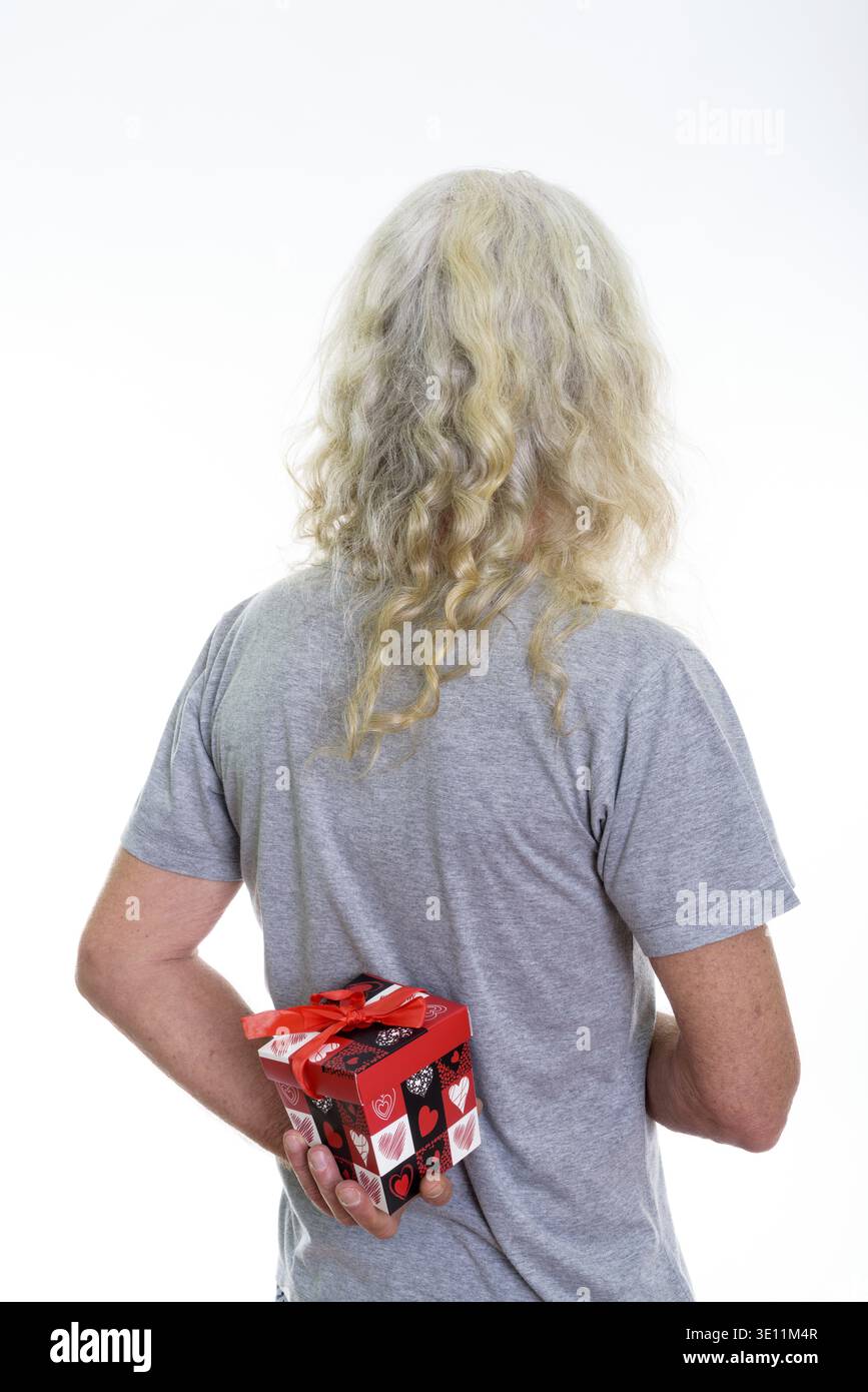 Back view of senior bearded man hiding red gift box behind back ready for Valentine's day Stock Photo