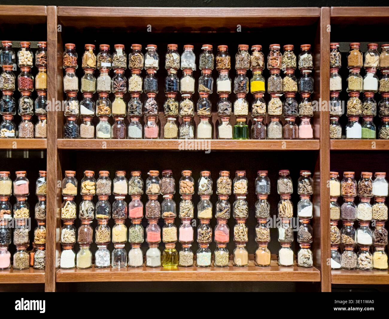 Several wooden shelves are stacked full of different glass spice jars filled with multi-colored spices and flavors in central Lima. Stock Photo