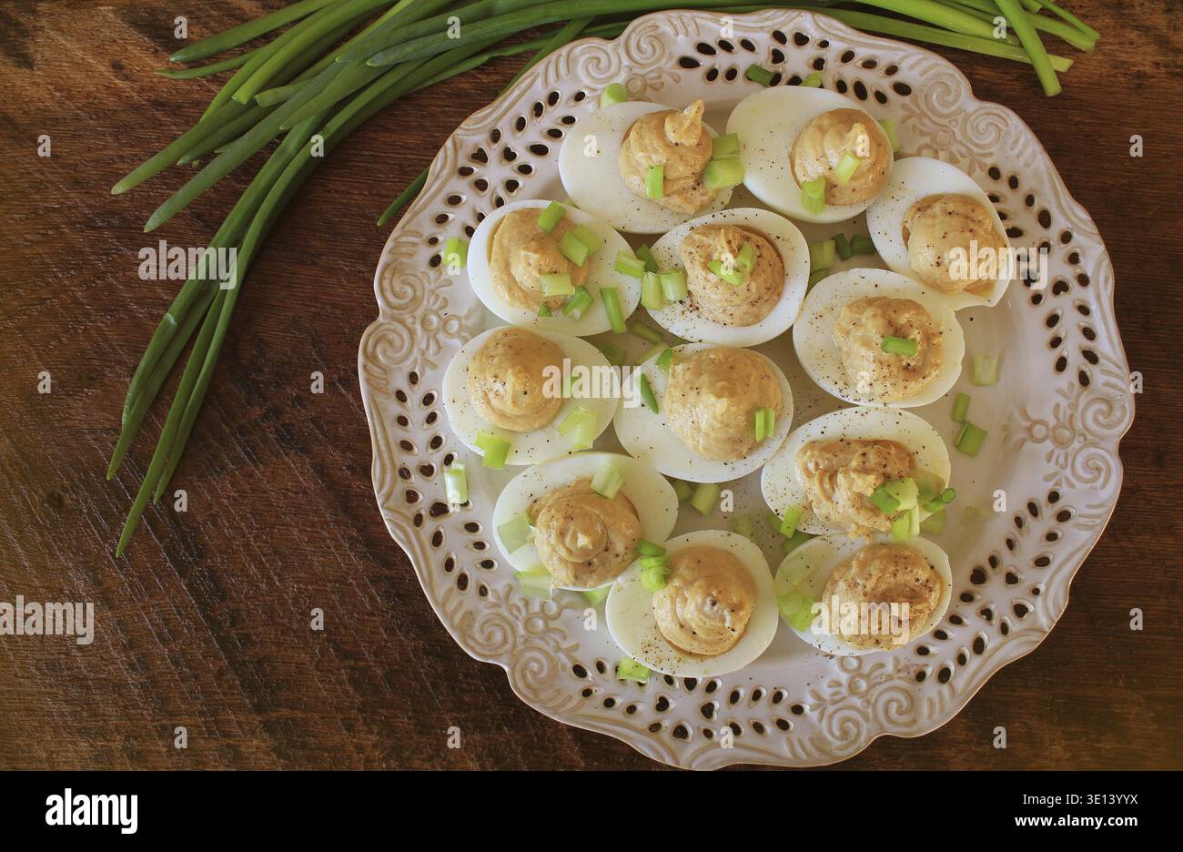 Deviled eggs with cod livers with leek on white plate. Rustic wooden table Stock Photo