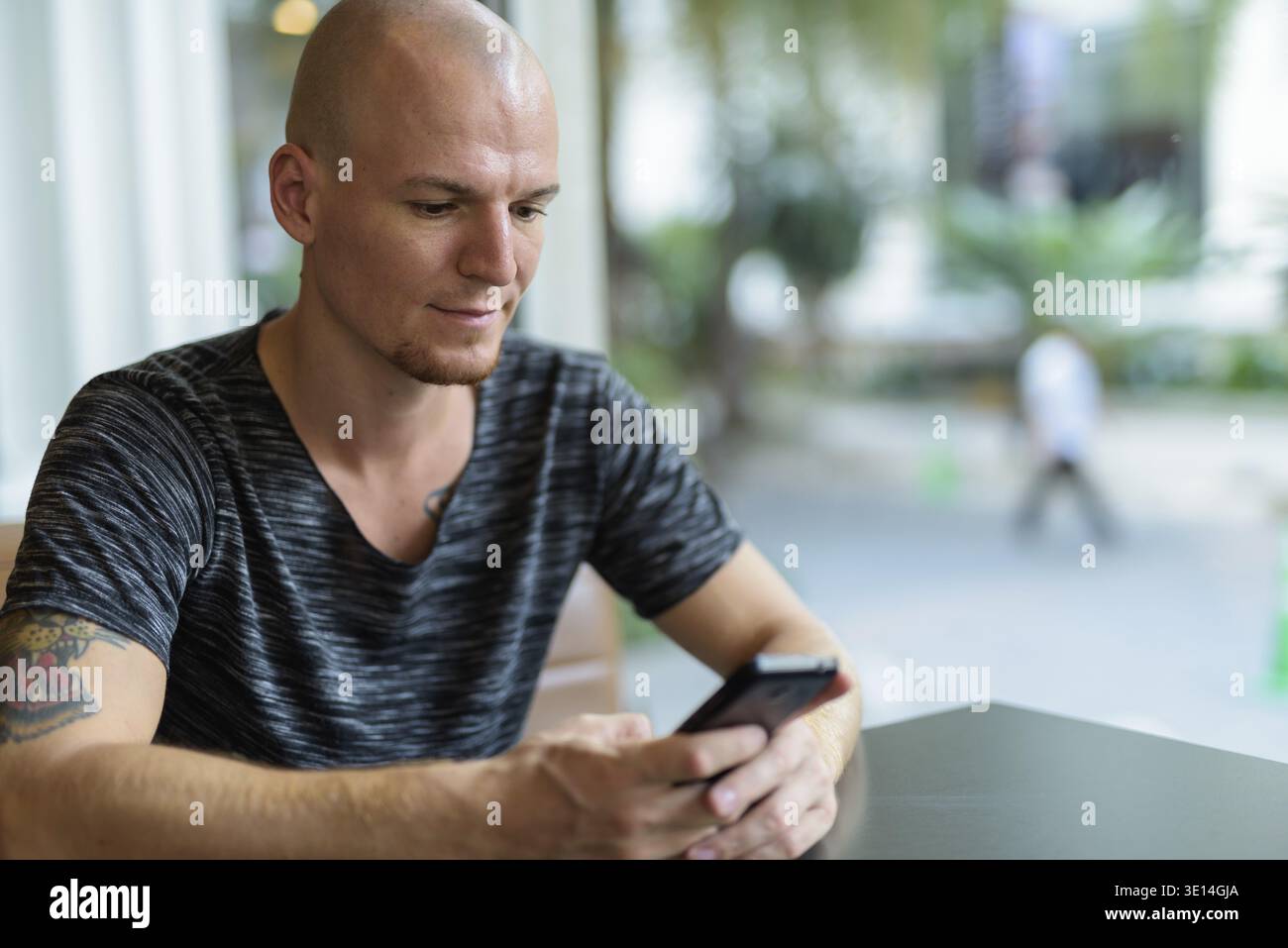 Young handsome bald man using mobile phone inside restaurant with glass windows Stock Photo