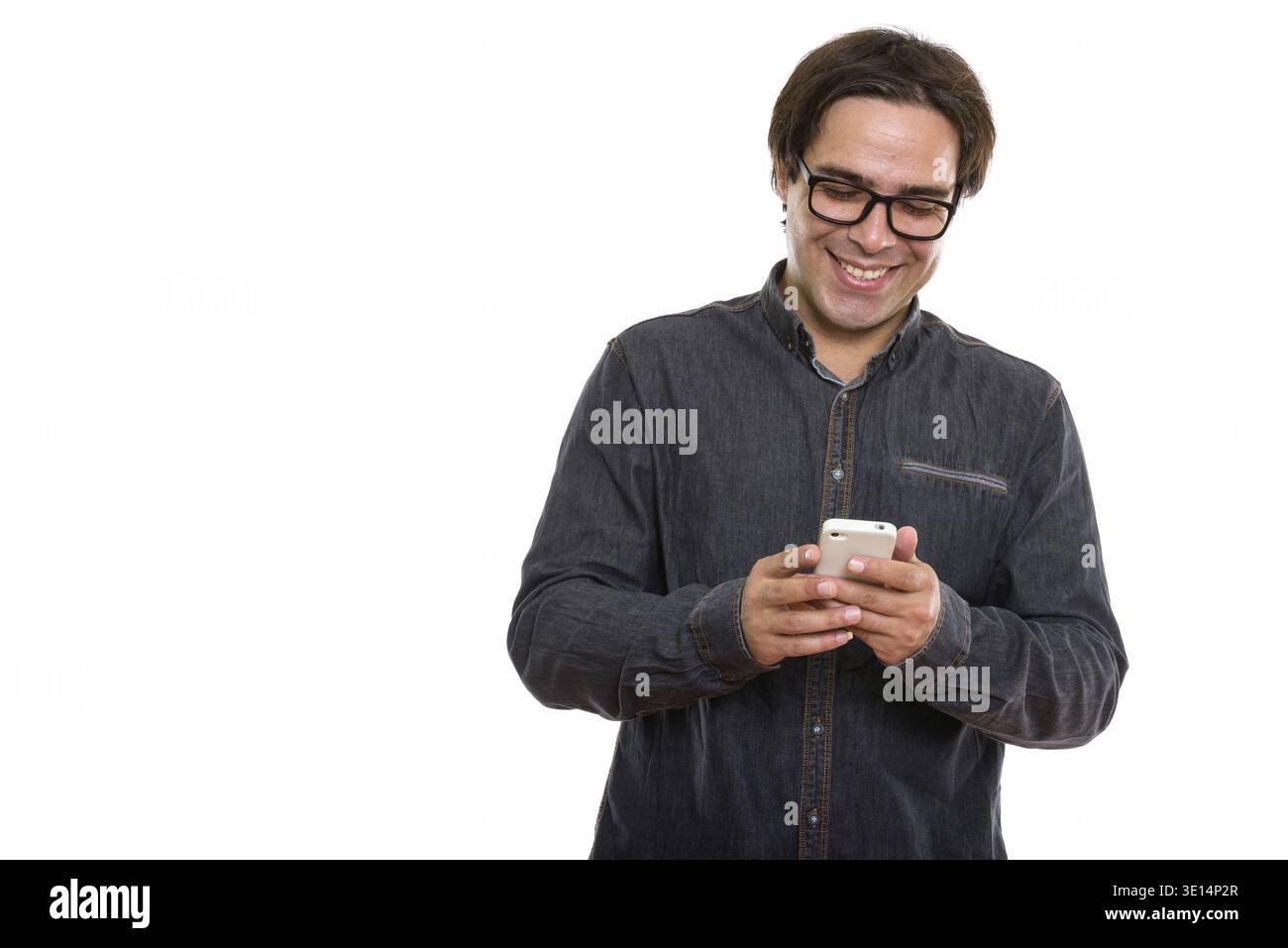 Studio shot of young happy Persian man smiling while using mobile phone Stock Photo