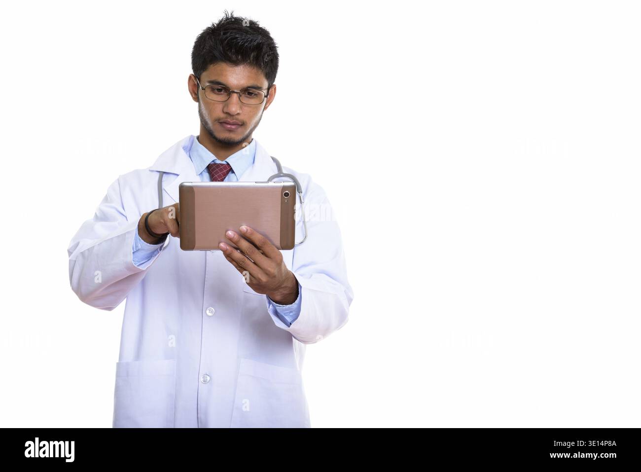 Studio shot of young handsome Indian man doctor using digital tablet Stock Photo