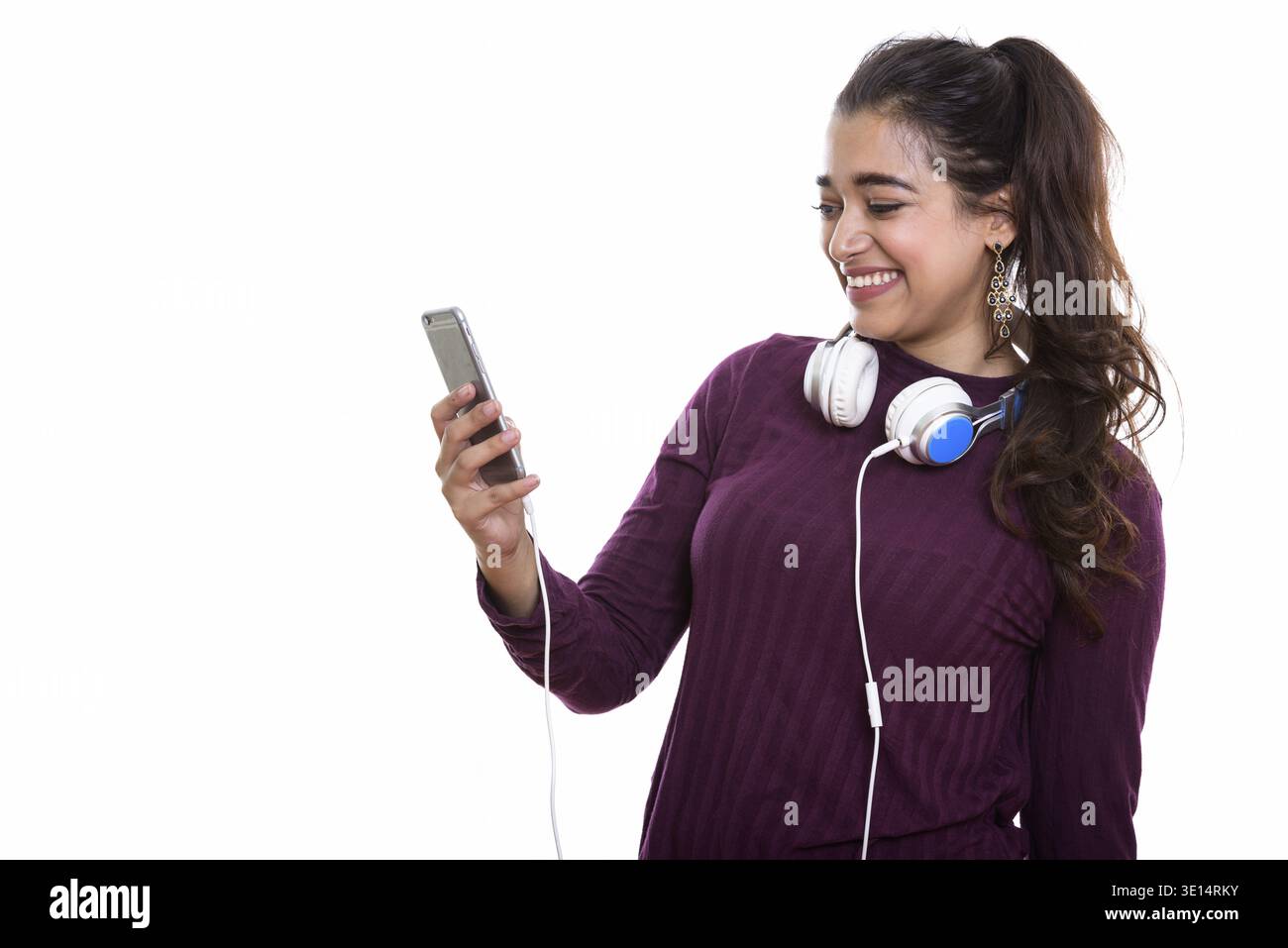 Young happy Indian woman smiling while wearing headphones around neck while using mobile phone Stock Photo