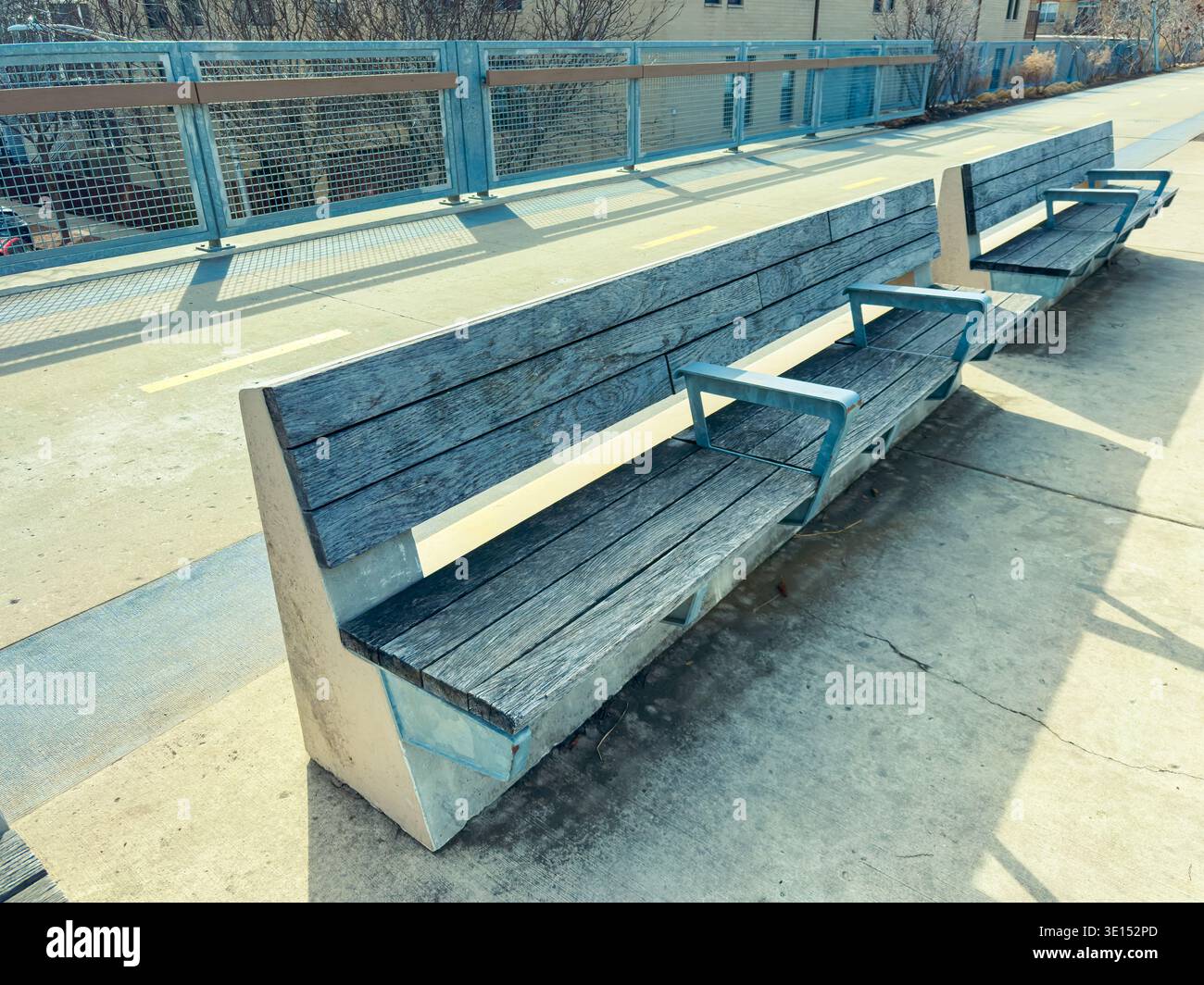 Two long wooden benches sit next to each other along a concrete walkway ...
