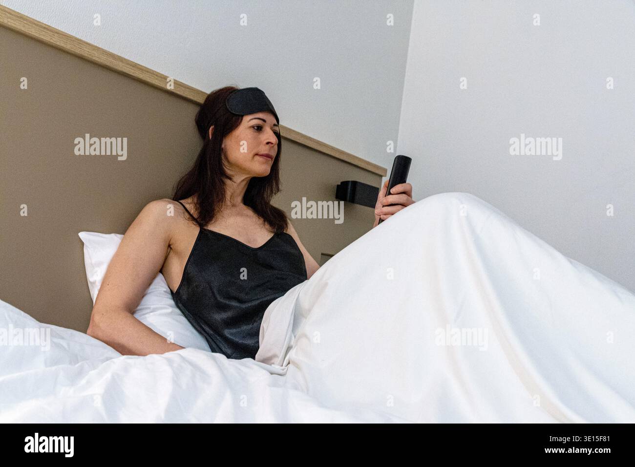 Woman preparing for sleep checking smart remote control Stock Photo