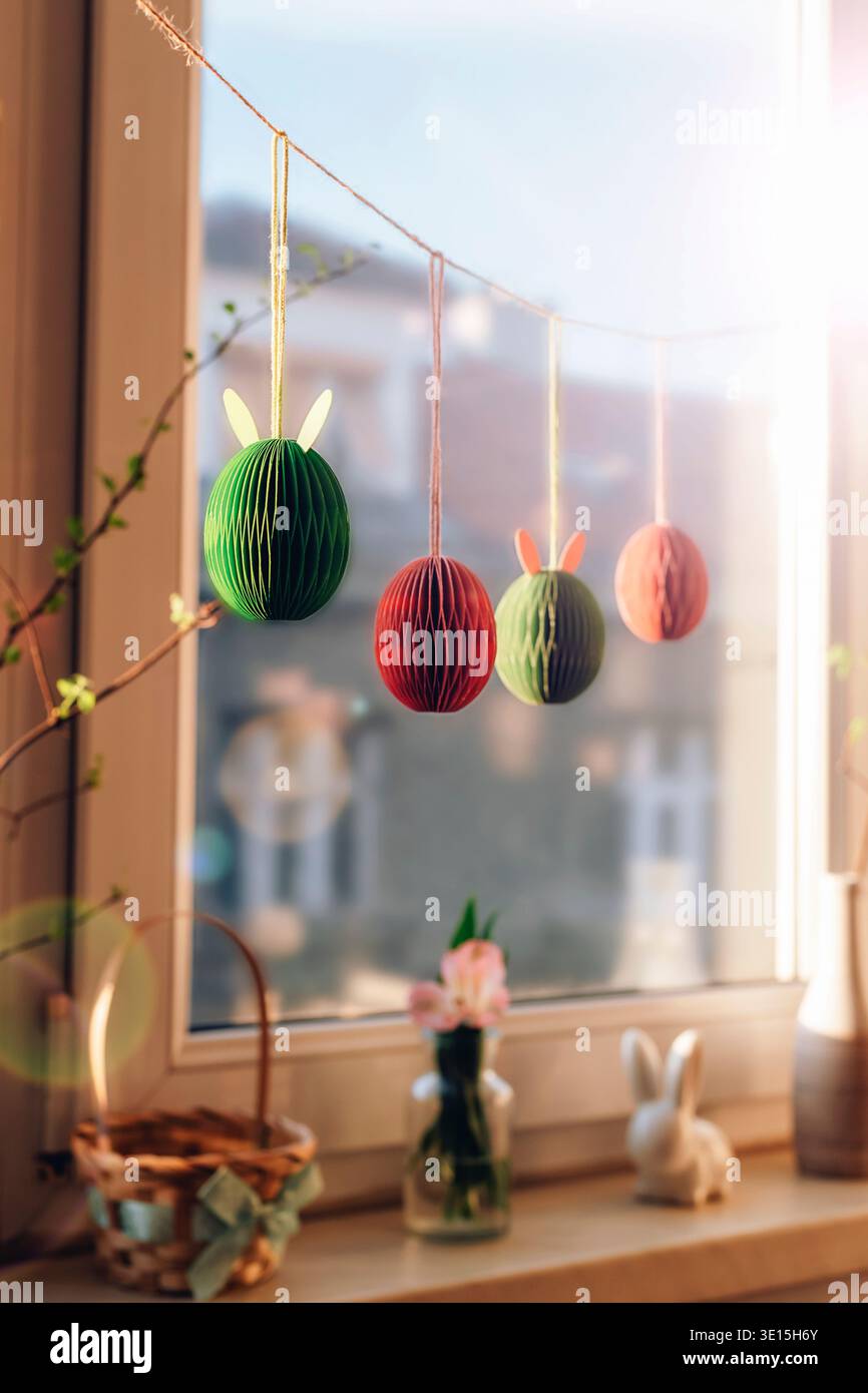 Paper Easter egg decorations hanging against window with sunlight. Selective focus. Stock Photo