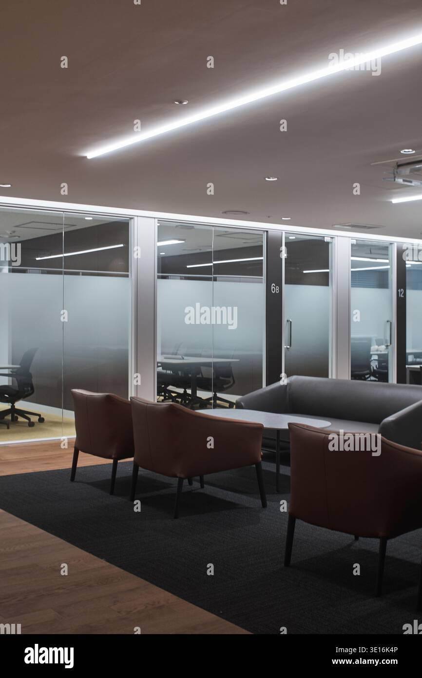 Moody office lounge with soft seating behind glass partitions. Stock Photo
