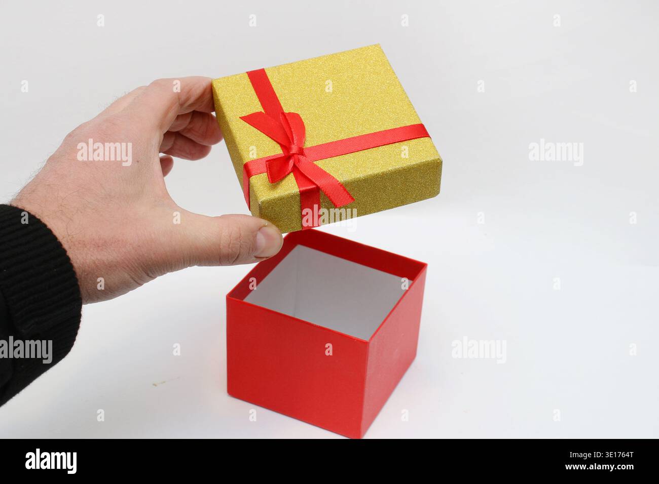 Hand opens the box against a clean white background. Red interior contrasts with shiny exterior. Simple, elegant, festive gesture for any occasion Stock Photo
