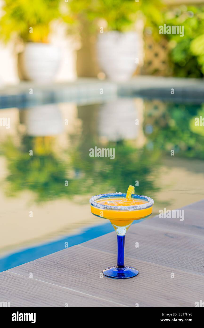 A vibrant orange cocktail sits elegantly beside a sparkling swimming pool,  capturing the essence of summer relaxation. The perfect setting for a leisu  Stock Photo - Alamy