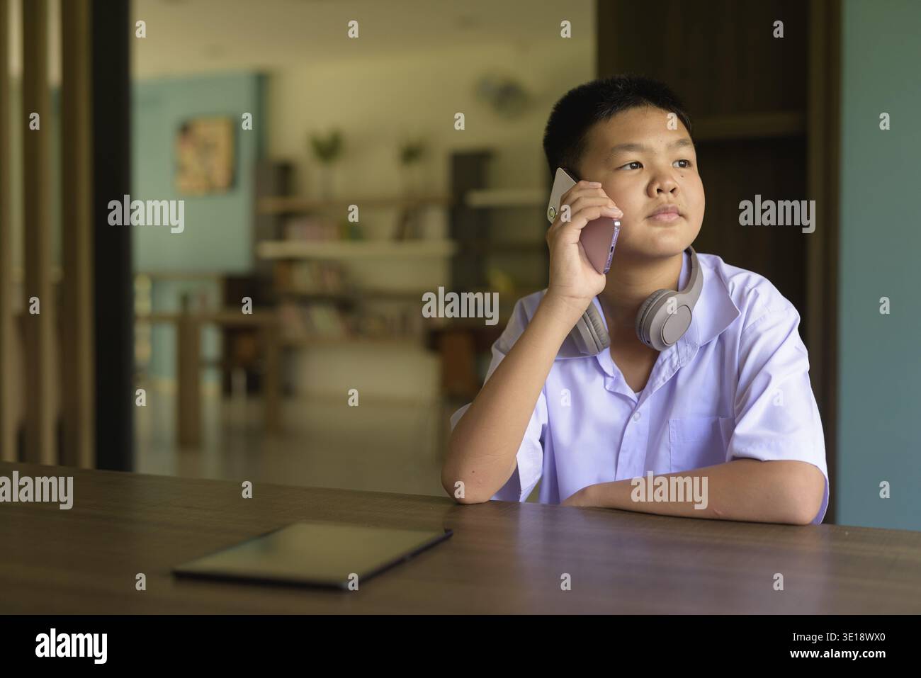 Thai Student in School Uniform Studying in Library Using Phone Stock Photo