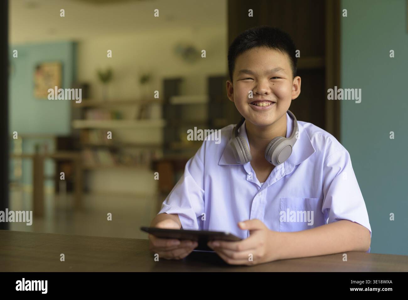 Thai Student in School Uniform Studying in Library Using Tablet Computer Stock Photo