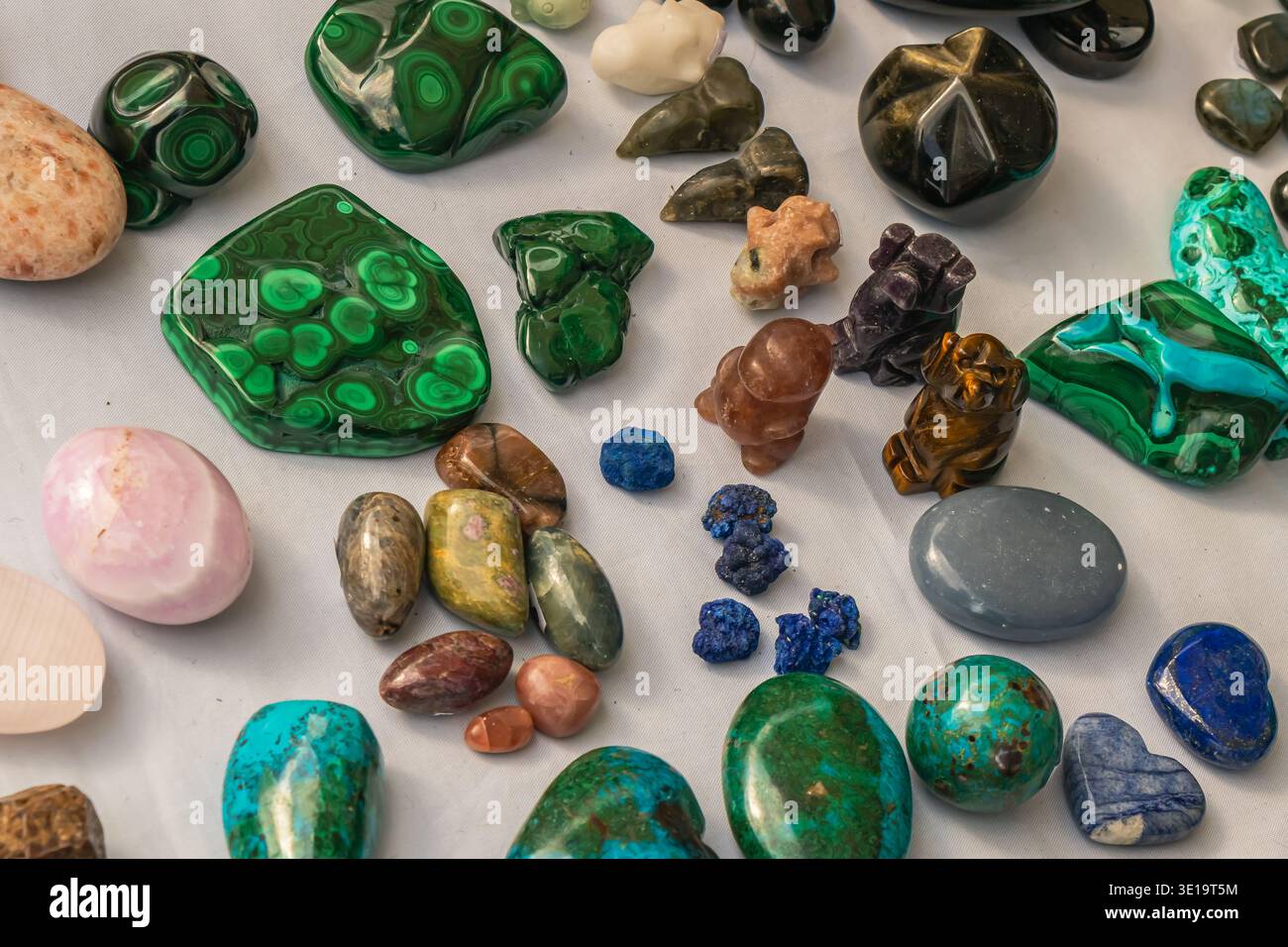 Flat lay view of polished gemstones and mineral pieces arranged on a white surface, featuring green malachite, turquoise stones and various colorful c Stock Photo