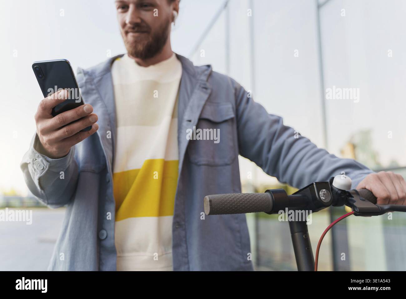 Young man with e-scooter using scooter-sharing system application on his smartphone Stock Photo