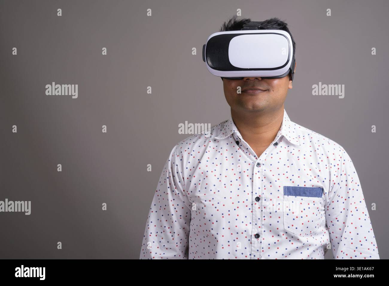 Studio shot of young Indian businessman using virtual reality headset against gray background Stock Photo