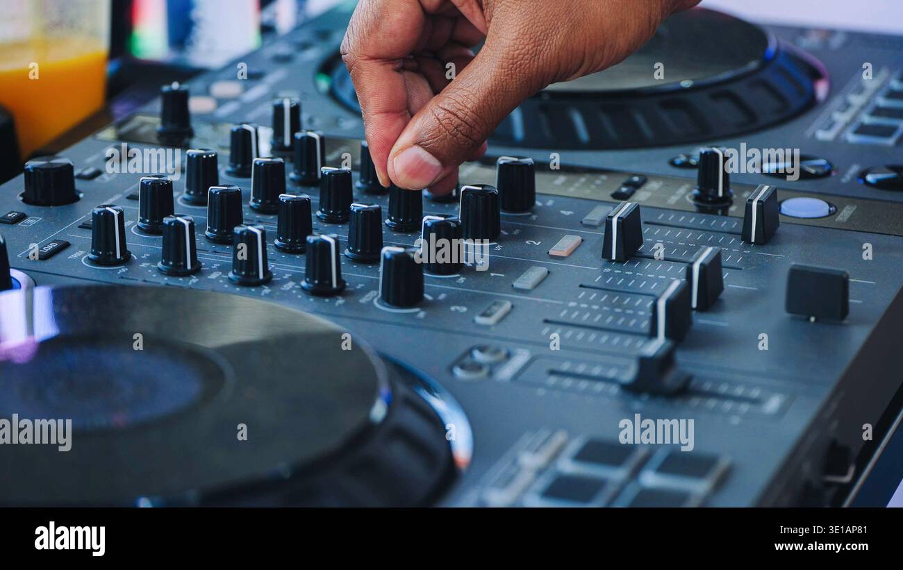 Hand adjusting controls on a DJ mixer controller, creating electronic music at a festival Stock Photo