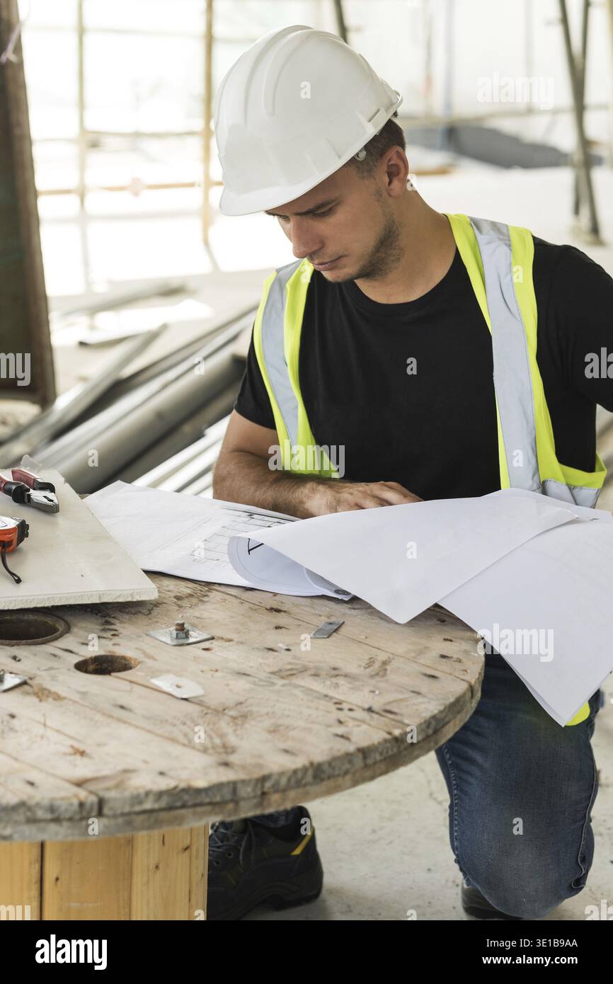 Young is worker checking blueprints during his work on a construction site Stock Photo