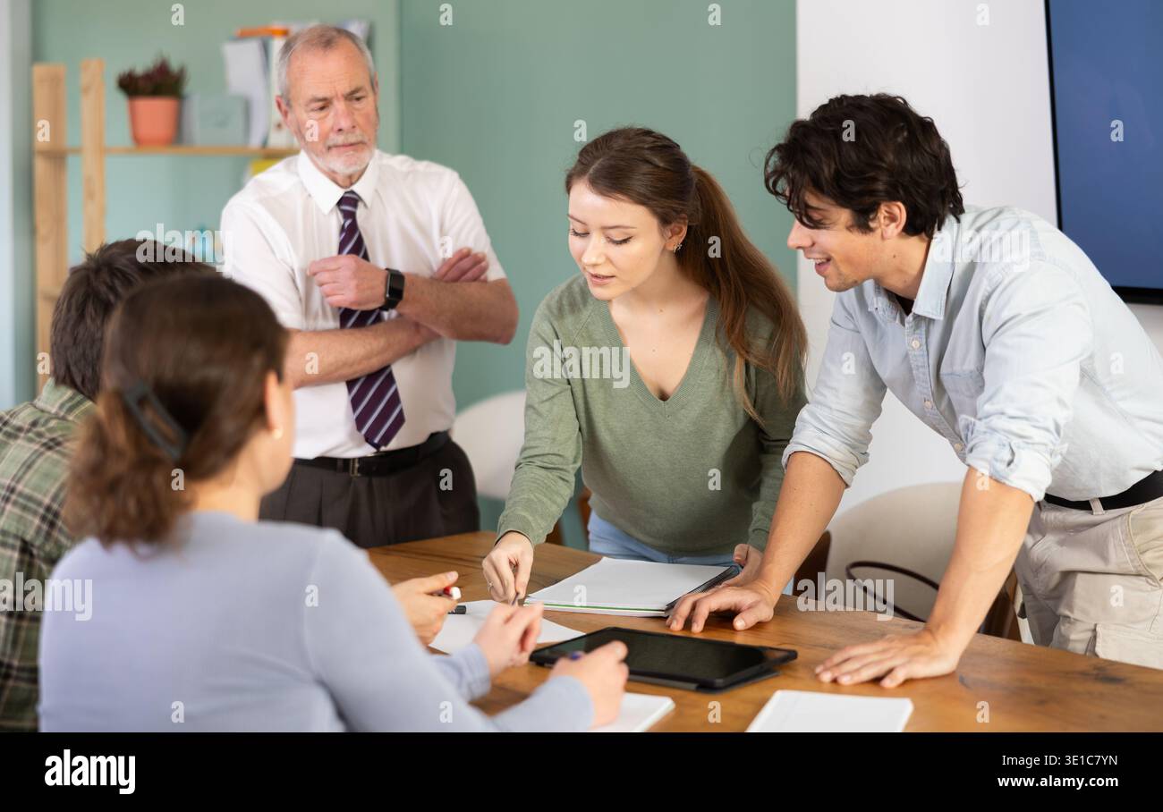 Students solving problems at table with teacher in background Stock Photo