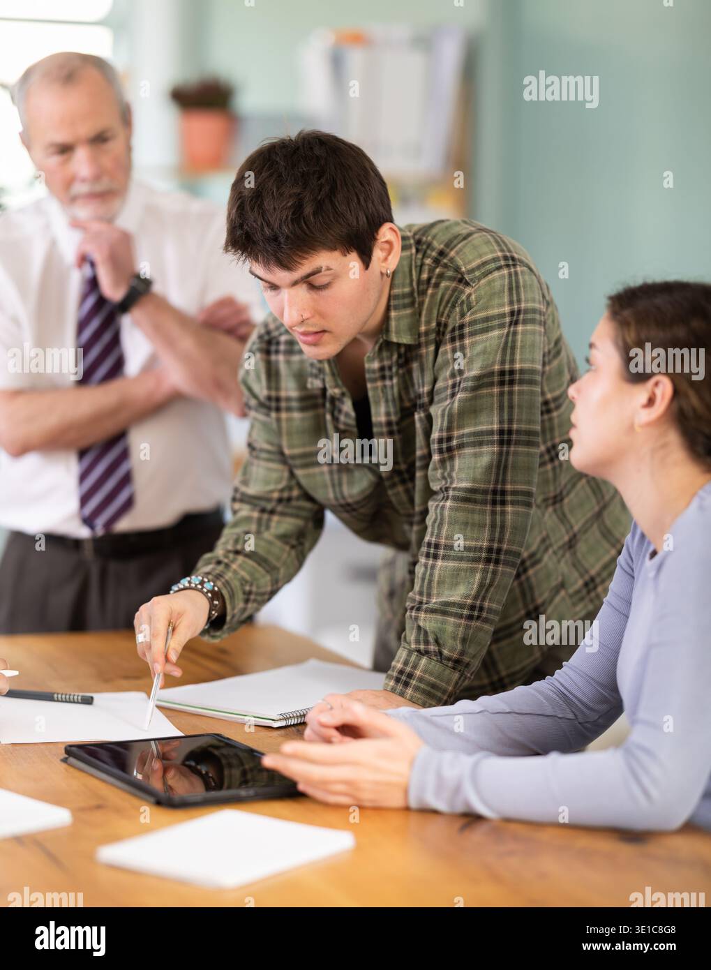 Students solving problems at table with teacher in background Stock Photo