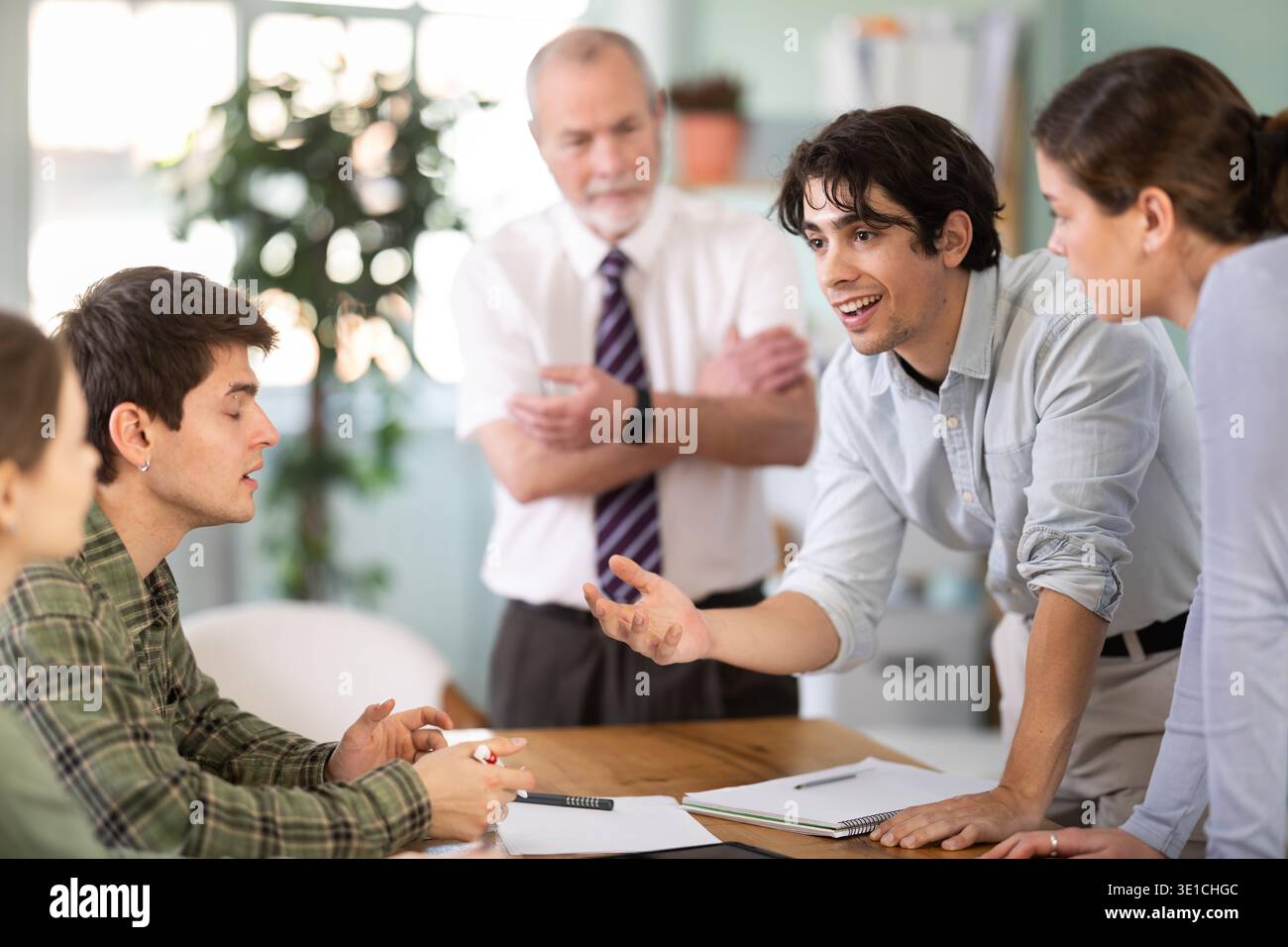 Students solving problems at table with teacher in background Stock Photo