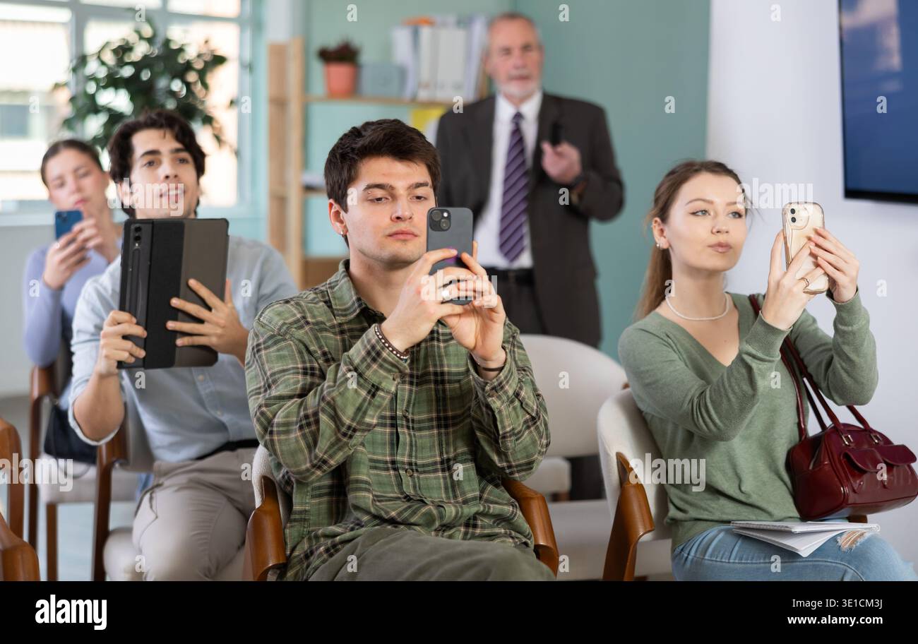 Students scanning QR code or taking photo, professor in background Stock Photo
