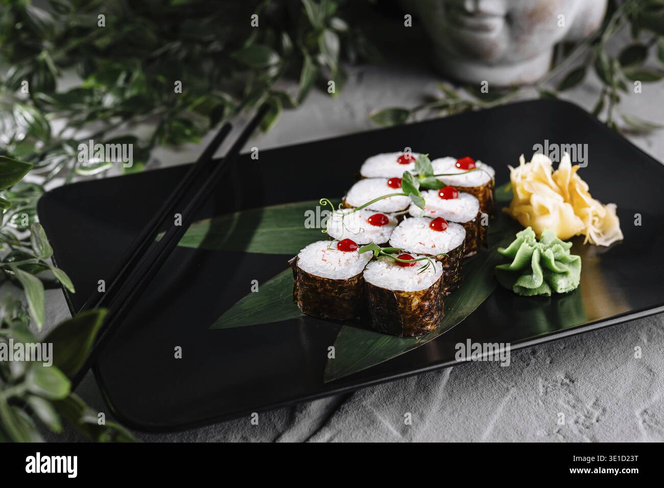Sushi rolls set served on black plate decorated with greenery and chopsticks Stock Photo
