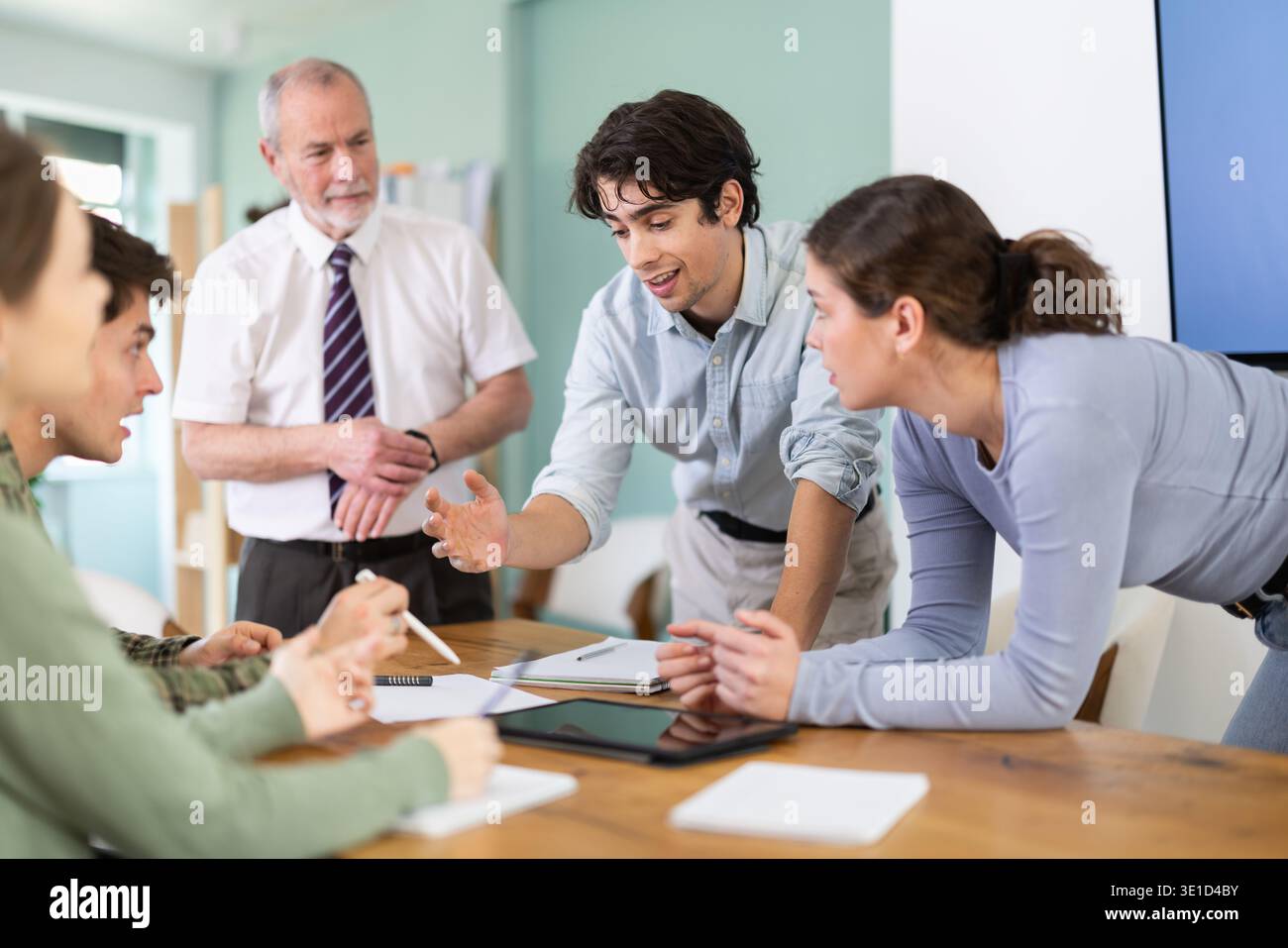 Students solving problems at table with teacher in background Stock Photo