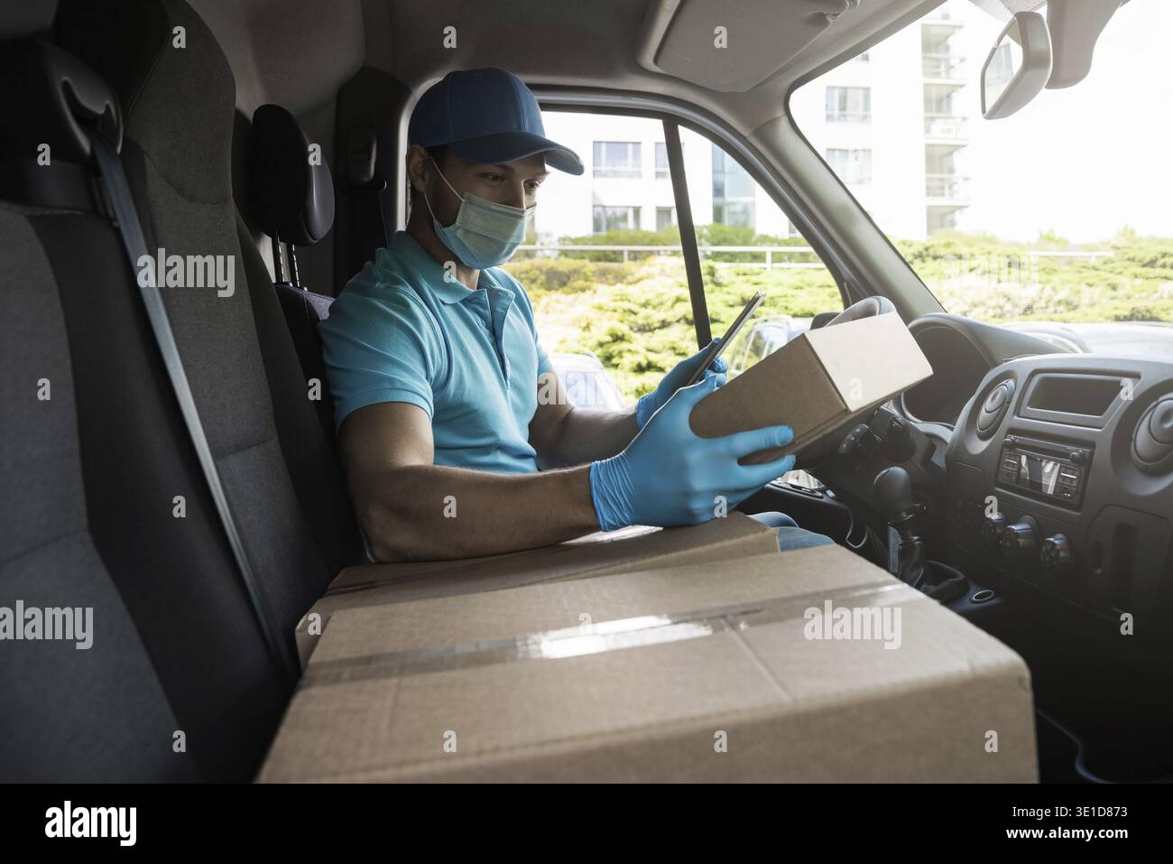 Young courier man in a van is checking packages and waybill using tablet pc before delivery Stock Photo