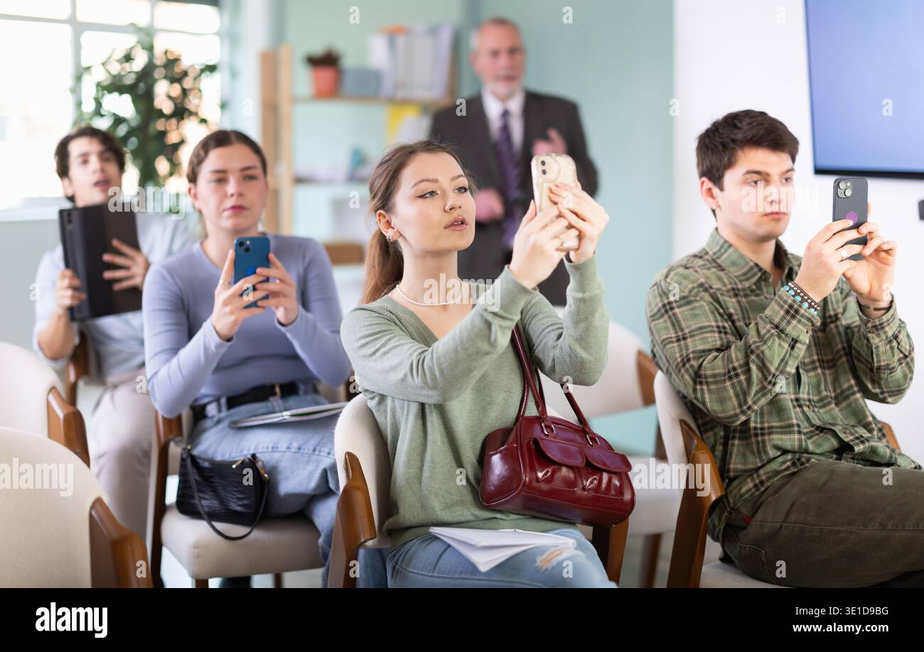 Students scanning QR code or taking photo, professor in background Stock Photo