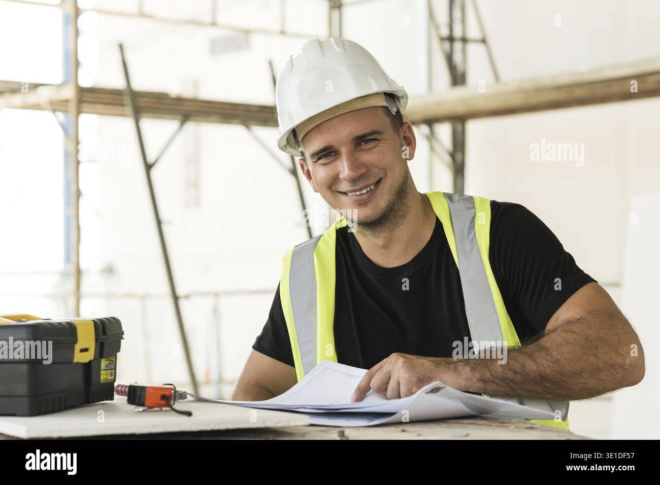 Young is worker checking blueprints during his work on a construction site Stock Photo