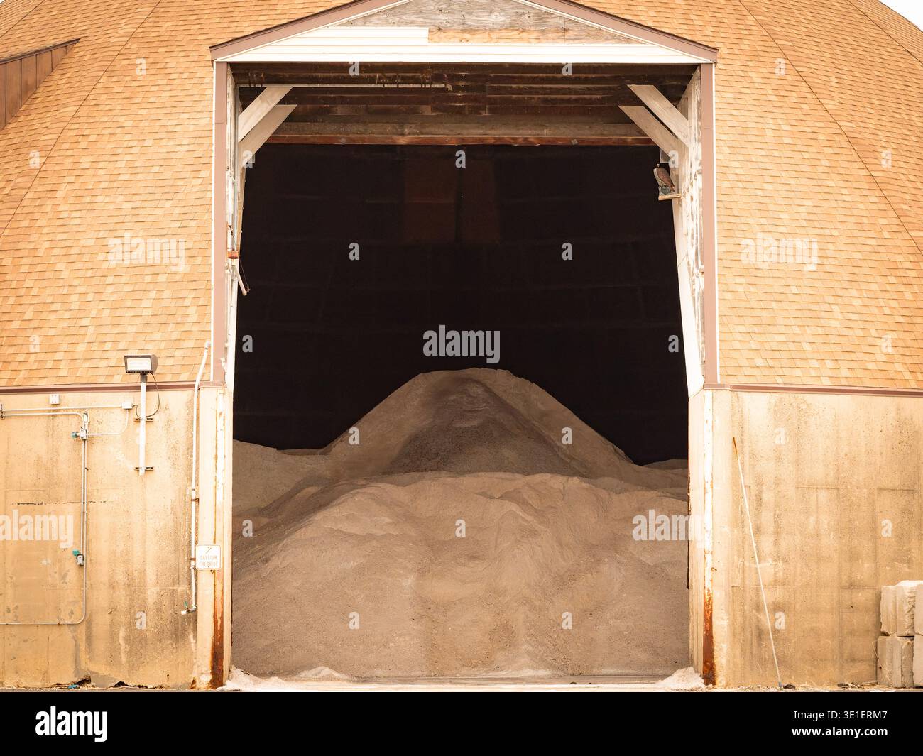 Large pile of calcium chloride or road deicer stored inside domed barn silo structure open doorway Stock Photo