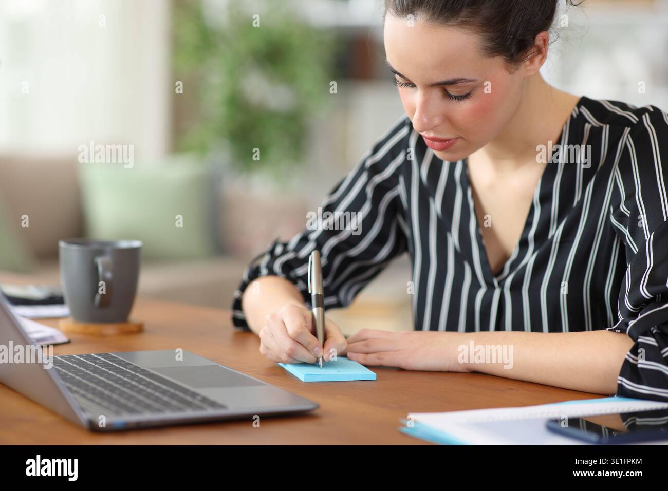 Self employed writing in blue sticky note on a wooden table working at home Stock Photo