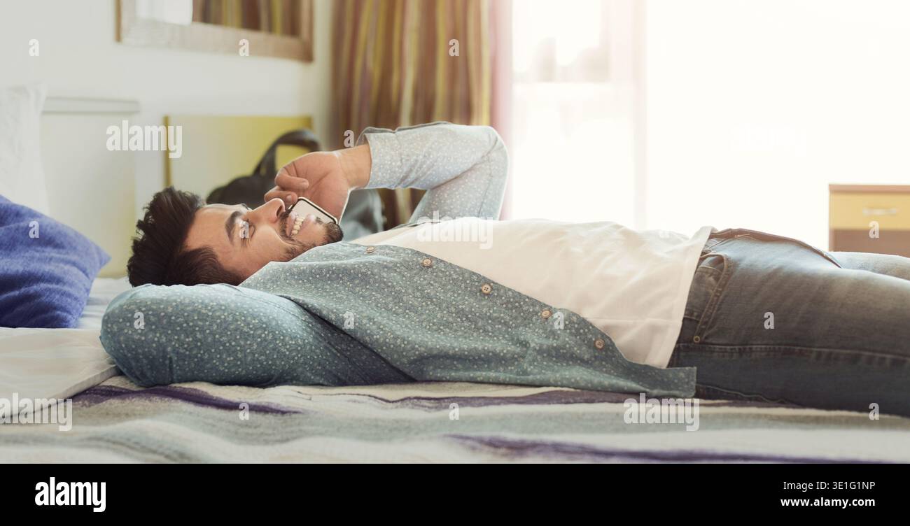 Young man talking on mobile phone while relaxing in bed Stock Photo
