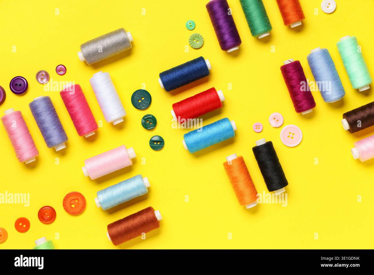 Composition with many different thread spools and buttons on yellow background Stock Photo