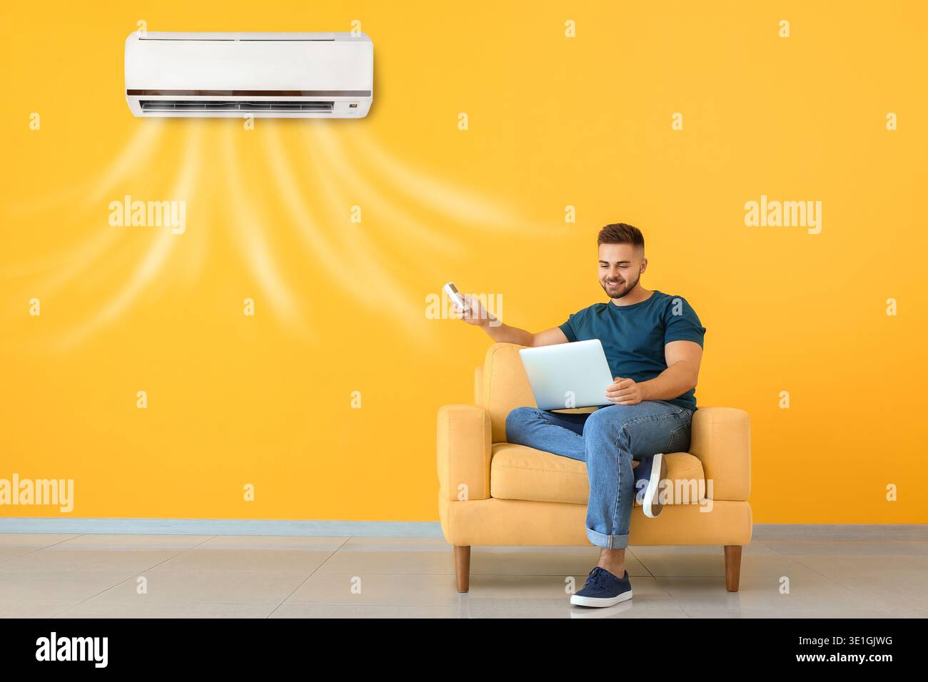 Young man with laptop switching on air conditioner at home Stock Photo