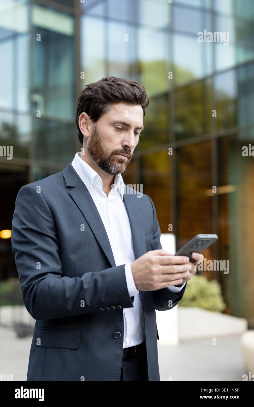 While Viewing Businessman viewing smartphone content while standing outdoors ...