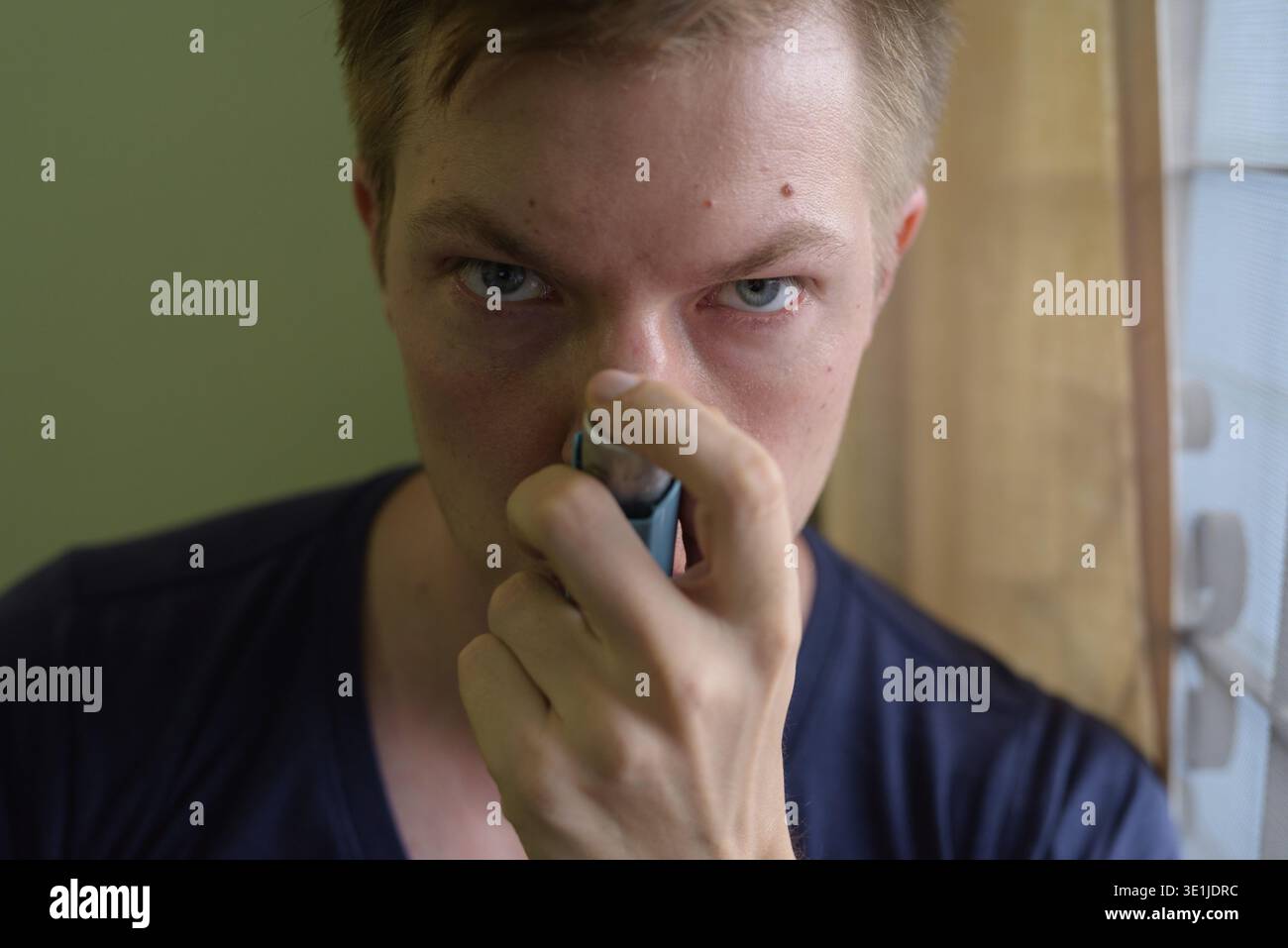 Portrait of young handsome man using asthma inhaler at home Stock Photo