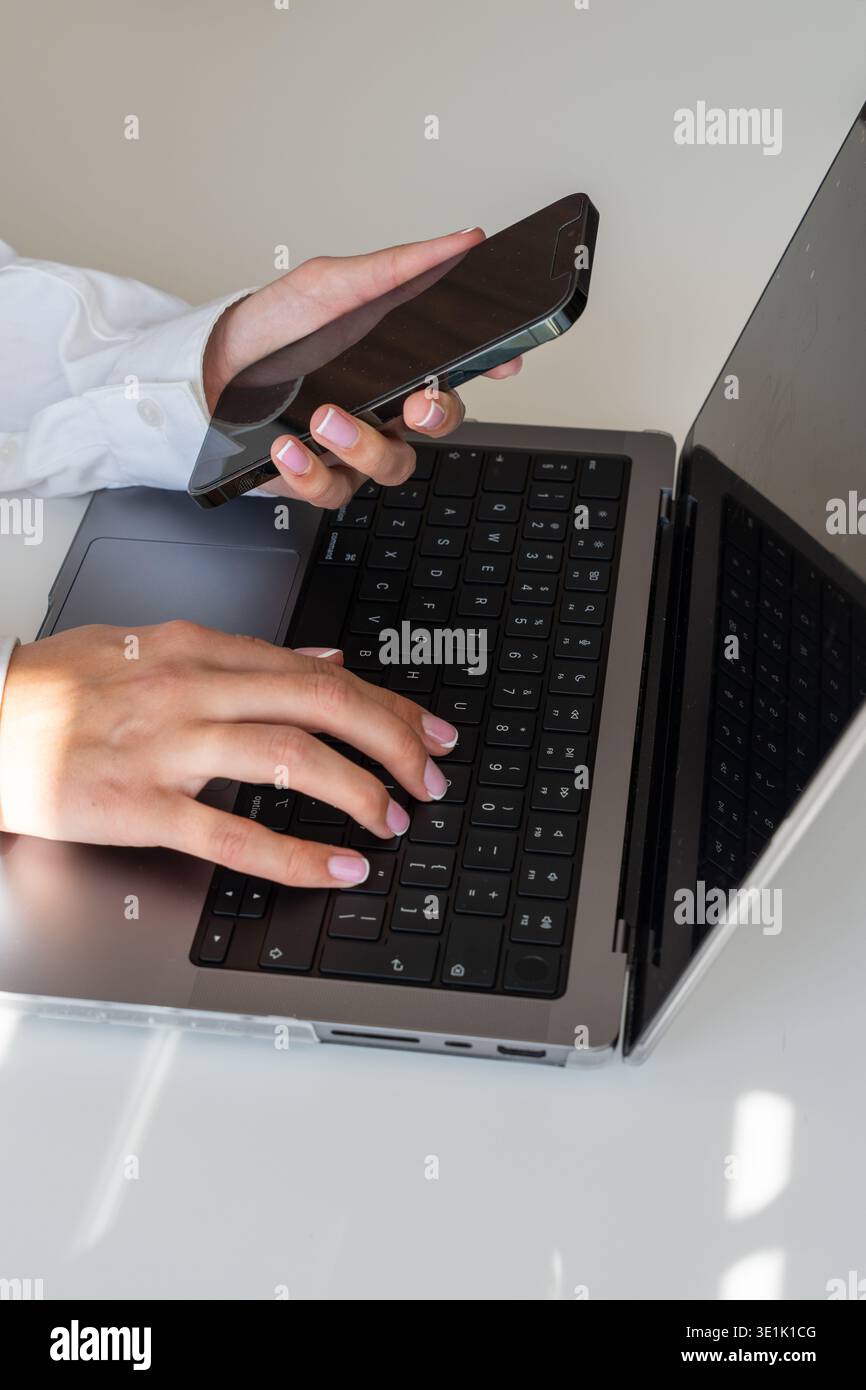 Digital Multi-Tasking – Female Hands in White Shirt Using Laptop and Phone in Natural Light Stock Photo
