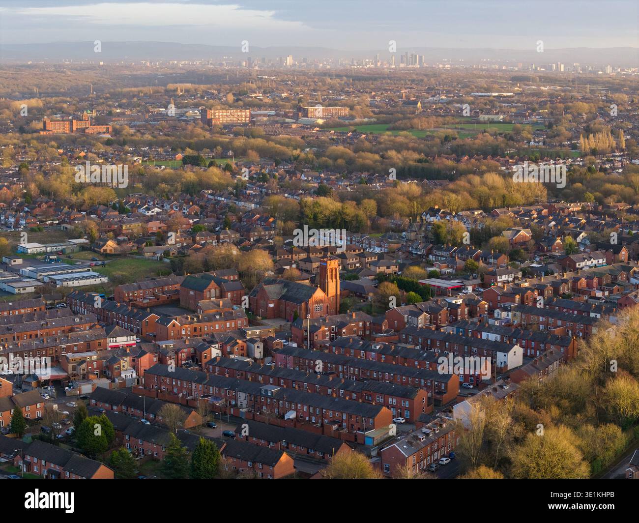 Aerial image looking southeast from Bolton toward the distant skyscrapers of Manchester and Salford, framed by lush suburban greenery. Stock Photo