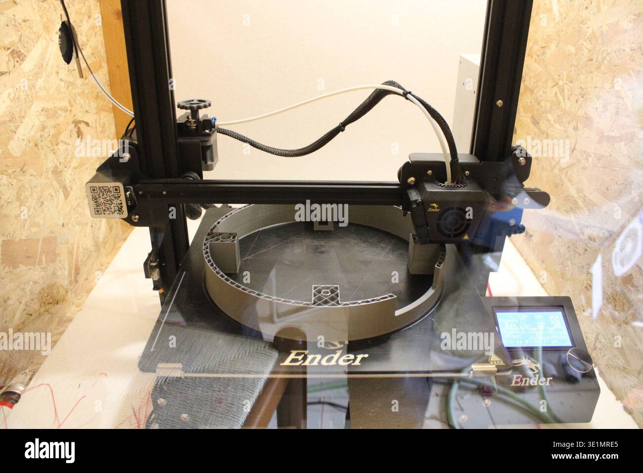 FDM 3D printer producing a plastic object layer by layer on the print bed, demonstrating additive manufacturing technology in a workshop environment. Stock Photo